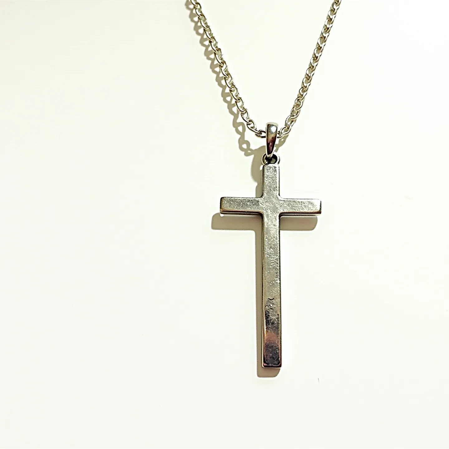 This faith necklace features a sleek, metallic cross pendant that is suspended from a delicate chain. The cross, with its smooth and polished finish, indicates it may be crafted from a silvery metal, possibly stainless steel or silver. The pendant is attached to the chain by a simple circular bail that allows it to hang freely and move with ease. The chain appears to be a classic cable style, adding durability and subtle elegance to the overall design. There are no visible gems or stones adorning the cross, emphasizing its minimalist and timeless appeal.