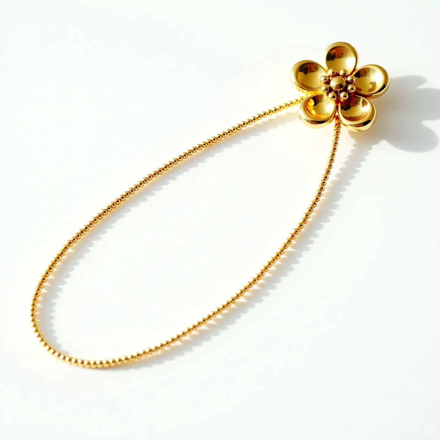 This flower necklace features a delicate gold tone, with a prominently crafted floral pendant characterized by five smoothly curved petals. The pendant's center is adorned with small, rounded embellishments, which add a touch of intricacy to the design. The necklace comprises a fine beaded chain that complements the flower motif, giving it a cohesive and elegant look. The design does not seem to include any visible gemstones, further emphasizing the metalwork. The necklace appears to be clasp-free, possibly designed as a slip-on piece, enhancing its simplicity and elegance.