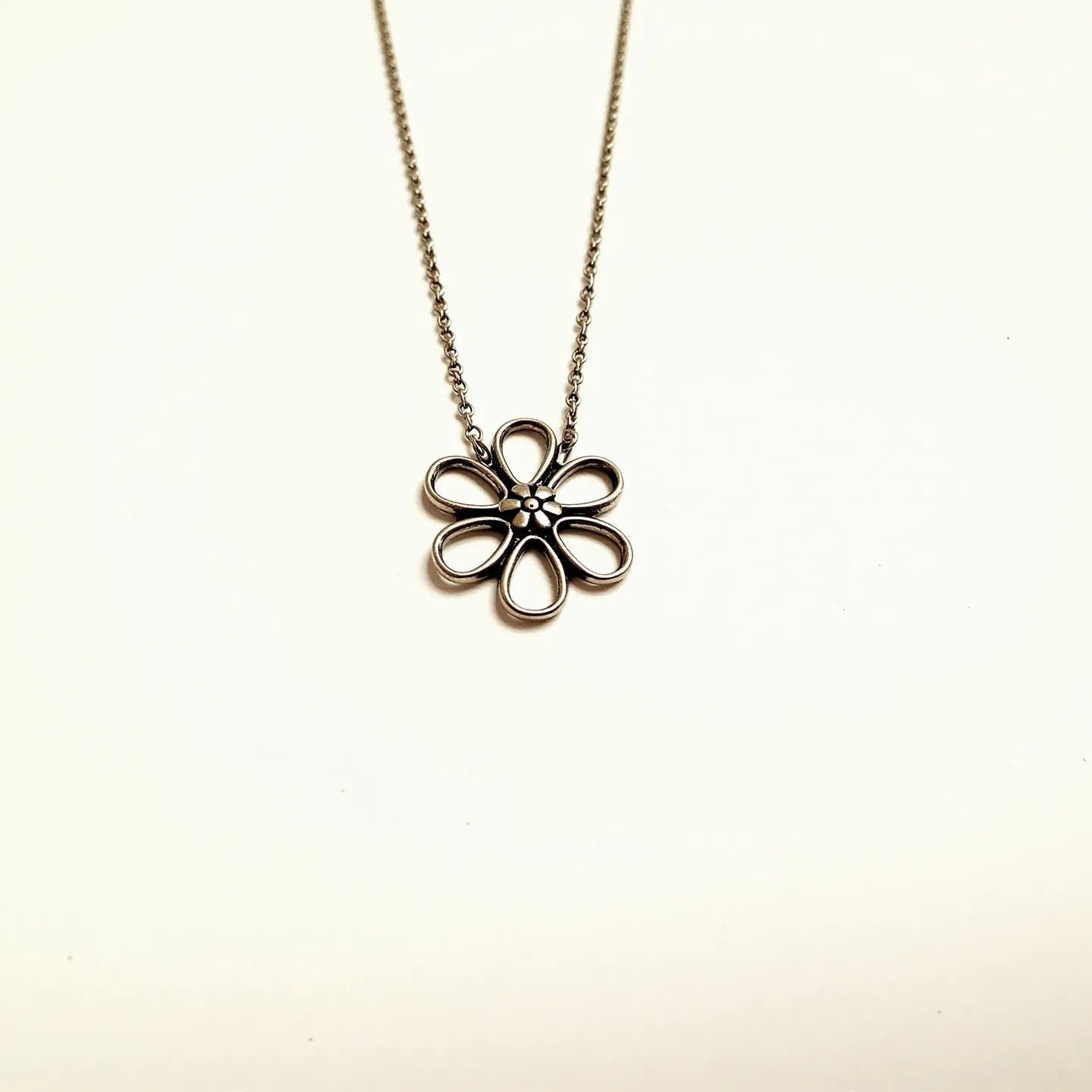 This flower necklace features a charming floral pendant crafted from a polished metal, likely silver or stainless steel, with a minimalist petal design. The petals form a circular shape around a small central bead, which may represent the pollen core of a flower. The petals themselves are open, creating a delicate and airy appearance. The necklace chain appears to be a fine link chain, matching the metal of the pendant, and offers a subtle complement to the floral design. The necklace is equipped with a standard clasp, likely a lobster or spring ring clasp, providing secure and easy attachment and removal.