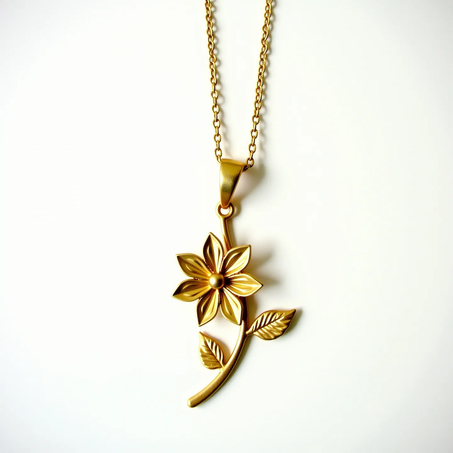 This flower necklace features a delicate design crafted from gold-toned metal, emphasizing an elegant and polished aesthetic. The pendant showcases an intricately formed flower with detailed petals, a smooth surface, and a central bead-like element that adds subtle dimension. The necklace is attached via a gold-toned chain that complements the pendant’s shine. The chain includes a sturdy clasp mechanism that ensures secure wear and ease of use. Elements of the design, such as the leaves and flower stem, enhance the organic motif, making this piece an elegant accessory.