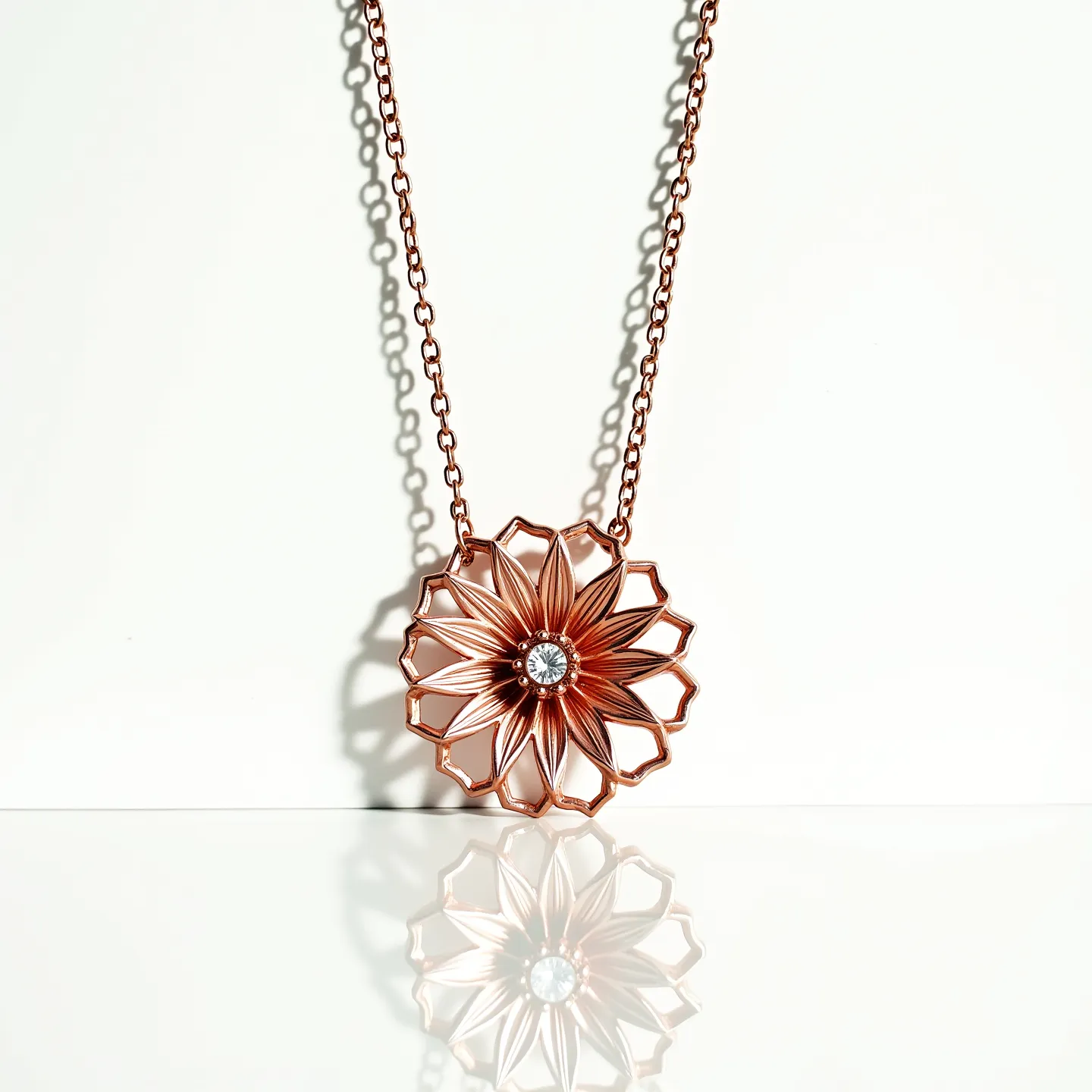 This flower necklace features a beautifully crafted floral pendant made from rose gold-toned metal, designed with delicate petal details that create an intricate pattern. At the center of the flower is a round-cut gem, likely a diamond or a similarly clear stone, set securely in a prong setting that highlights its brilliance. The pendant is suspended on a fine, matching rose gold-tone chain, which adds to the harmonious and elegant aesthetic of the piece. The necklace is completed with a simple lobster clasp, ensuring a secure and adjustable fit for the wearer.