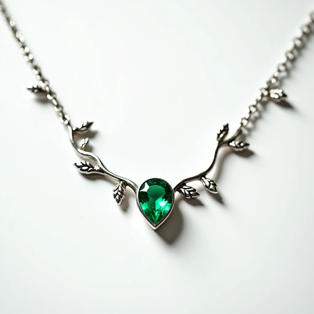 This gemstone necklace features a central teardrop-shaped green gemstone, likely an emerald or a similar stone, set in a sleek metal setting. The necklace is designed with silver-toned metal that forms an elegant branch motif adorned with small leaf elements, elegantly framing the stone. The chain links are uniform and complement the organic design, adding to the overall aesthetic. The necklace is completed with a discreet clasp that ensures a secure fit, allowing the intricate design to lay gracefully against the wearer's neckline.