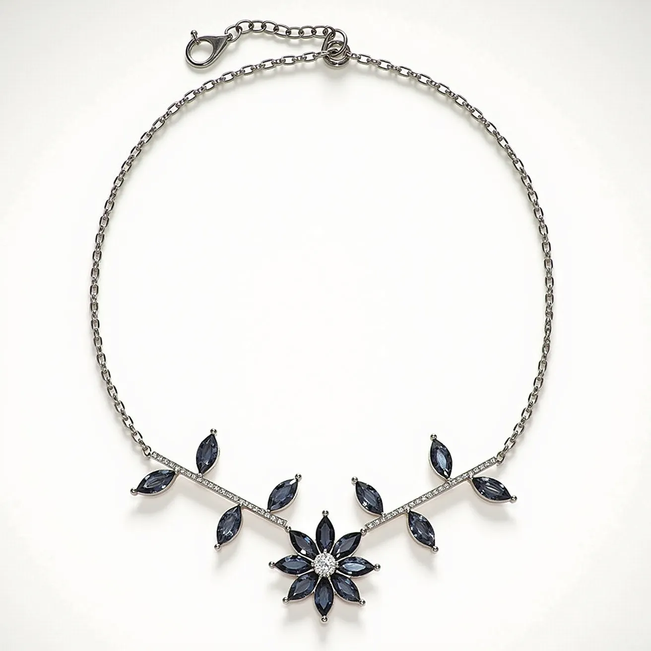 This gemstone necklace features a central floral design, incorporating dark blue, marquise-cut gemstones set elegantly into a silver-toned metal framework. Each petal of the flower and accompanying leaf-like structures display meticulous craftsmanship, emphasizing the symmetrical arrangement of the gems. The necklace is composed of a fine chain, complementing the intricate design of the pendant, and includes a simple lobster claw clasp for secure fastening. The combination of the dark stones with the metallic sheen of the setting creates a striking balance, making it a sophisticated accessory.