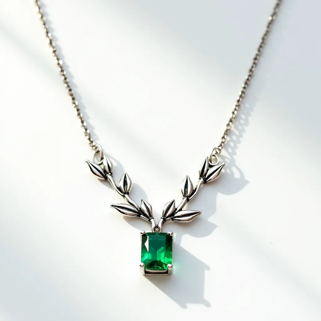 This gemstone necklace features a striking rectangular emerald-cut green stone set in a prong setting, which enhances its brilliance and visibility. The stone is suspended from a delicate chain that includes decorative metal leaves, creating an elegant nature-inspired motif. The chain appears to be made of a silver-toned metal, providing a contrasting backdrop that highlights the vivid color of the gemstone. The necklace fastens securely with a classic clasp, ensuring both functionality and style.