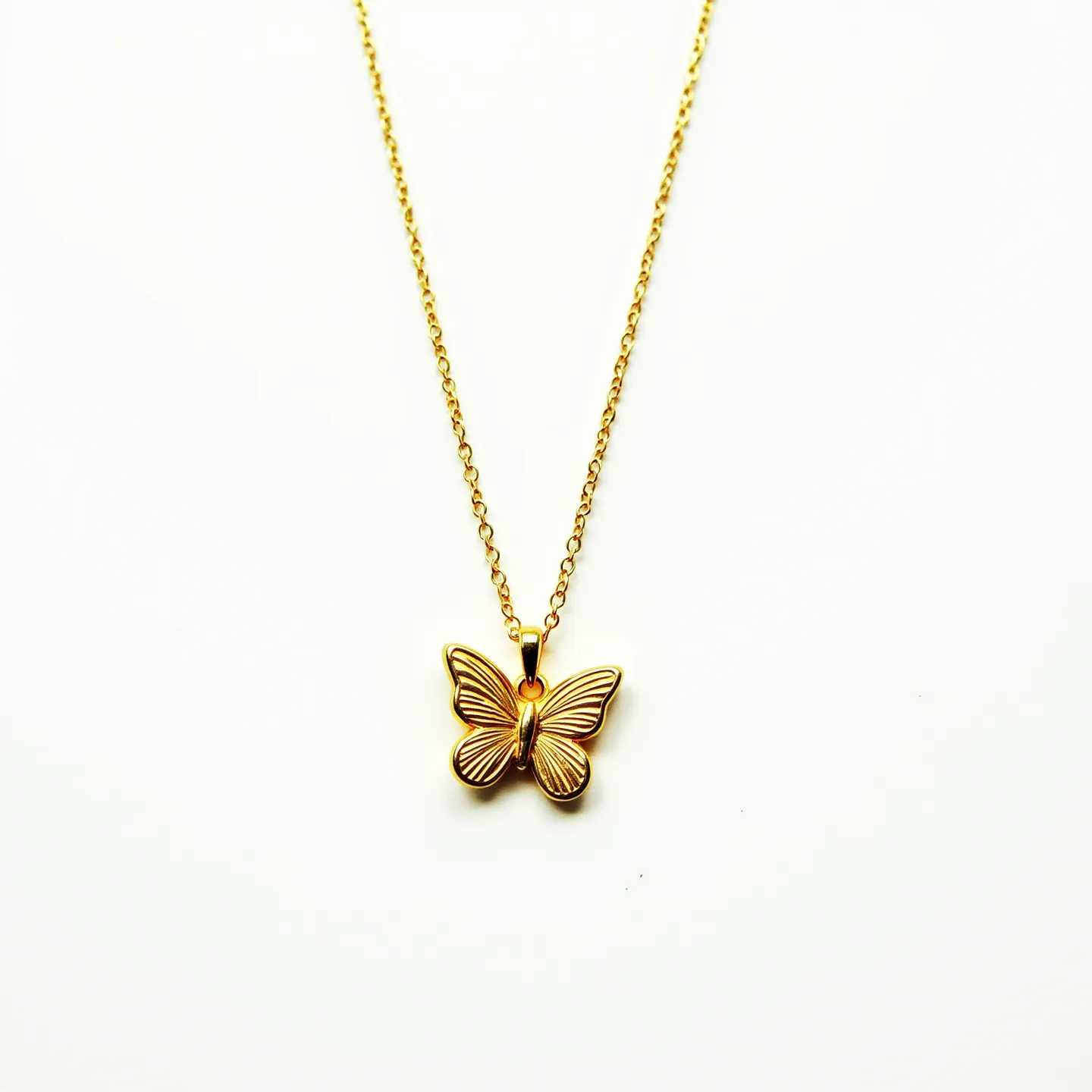 This girl's necklace features a delicate gold chain holding a charming butterfly pendant, likely crafted from metal with a polished gold finish. The butterfly pendant is detailed with engraved lines, adding texture and a sense of movement to the piece. The pendant hangs from the chain via a small, smooth loop that blends seamlessly with the chain. The necklace is completed with a small lobster clasp, ensuring a secure closure. The overall design is simple yet elegant, making it versatile for various occasions.