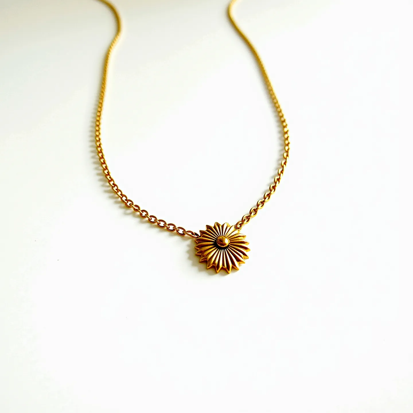 This girl's necklace features a delicate chain made of gold-toned metal. The centerpiece is a sunburst design, crafted from the same gold-tone material, exhibiting intricate detailing with petal-like extensions radiating outwards. At the core of the sunburst is a small, round bead that matches the overall gold hue, adding a minimalist but elegant touch. The necklace likely closes with a standard clasp, although it's not visible, ensuring a secure fit around the neck. The design is simple yet sophisticated, making it a versatile accessory.