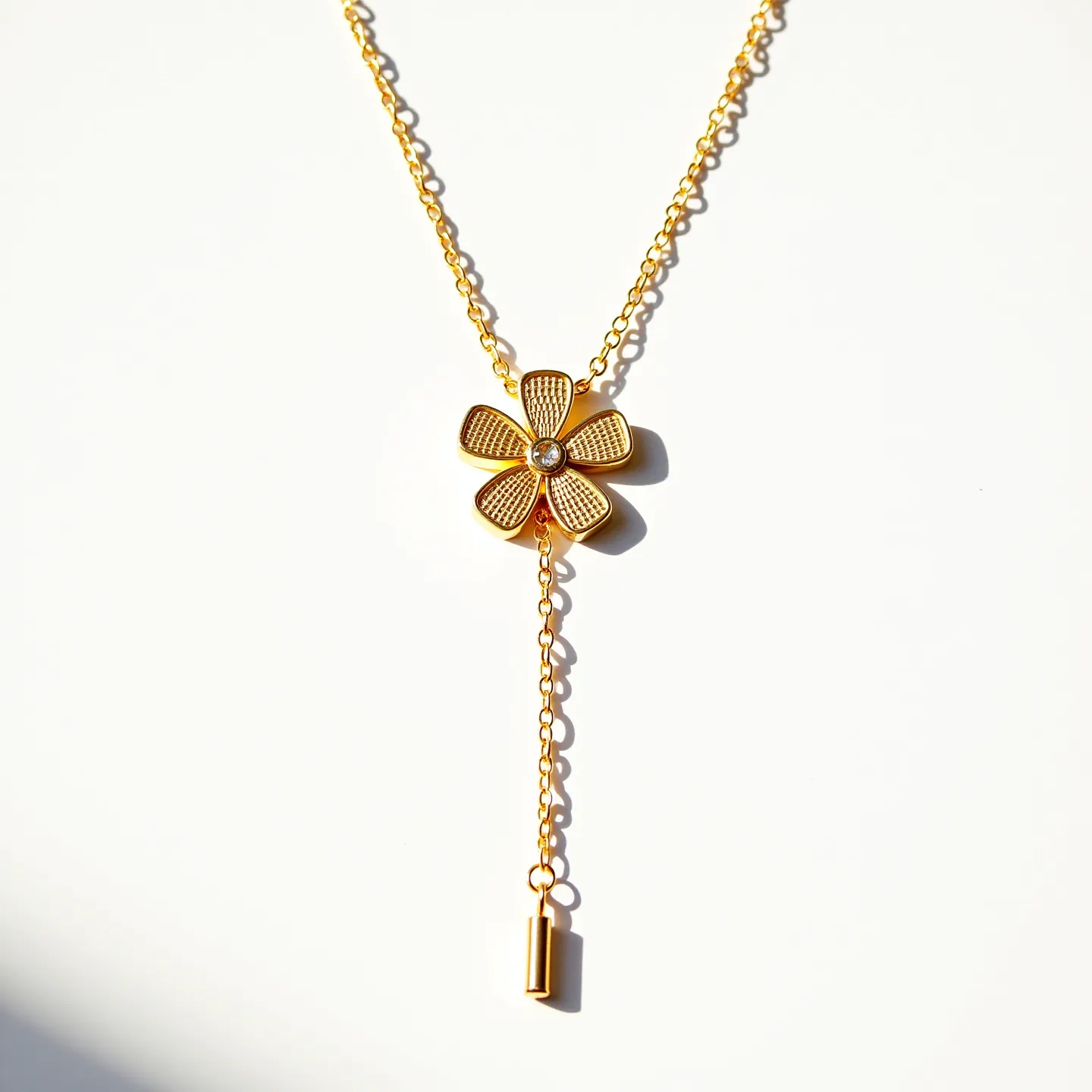 This girl's necklace features a delicate gold chain that carries a central flower-shaped pendant. The flower is crafted from gold, with intricate textured petals surrounding a single, round-cut gem in the center, likely a clear stone such as a diamond or cubic zirconia, set in a bezel setting. The chain is composed of small, uniform links that support the pendant and extend into a lariat style, with an elongated gold charm hanging from the bottom. The necklace is completed with a traditional clasp, which secures the piece around the neck.