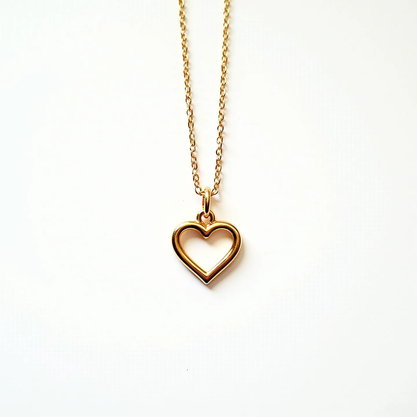 This girl's necklace features a delicate gold chain, composed of small, interlocking links that provide a simple yet elegant look. The pendant, crafted in the shape of a heart, is also gold, adding a consistent and harmonious touch to the necklace. The heart pendant is a hollow design, emphasizing the minimalist aesthetic of the necklace. Attached to the chain through a small loop, the pendant hangs gracefully. The closure likely features a typical clasp such as a lobster or spring ring, which would ensure both security and ease of use while wearing.