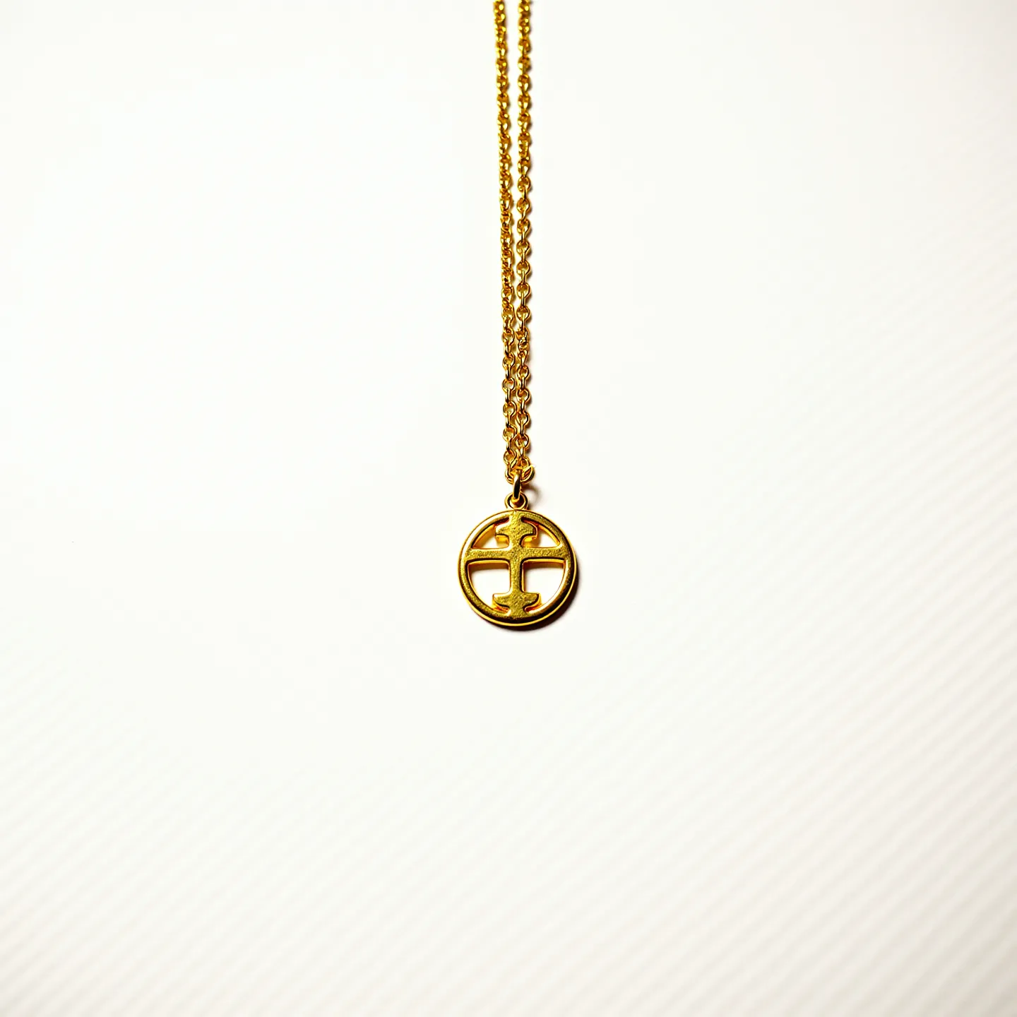 This gold chain features a simple, elegant design with fine links that support a circular pendant. The pendant showcases a polished gold finish with no additional gems, characterized by a cutout pattern that forms a cross-like motif. The chain appears lightweight, suggesting it is made from a delicate yet sturdy material, likely to ensure comfort while worn. The attachment appears to involve a standard chain link connection, seamlessly attaching the pendant to the chain to prevent any visible clasp while maintaining the aesthetic appeal.