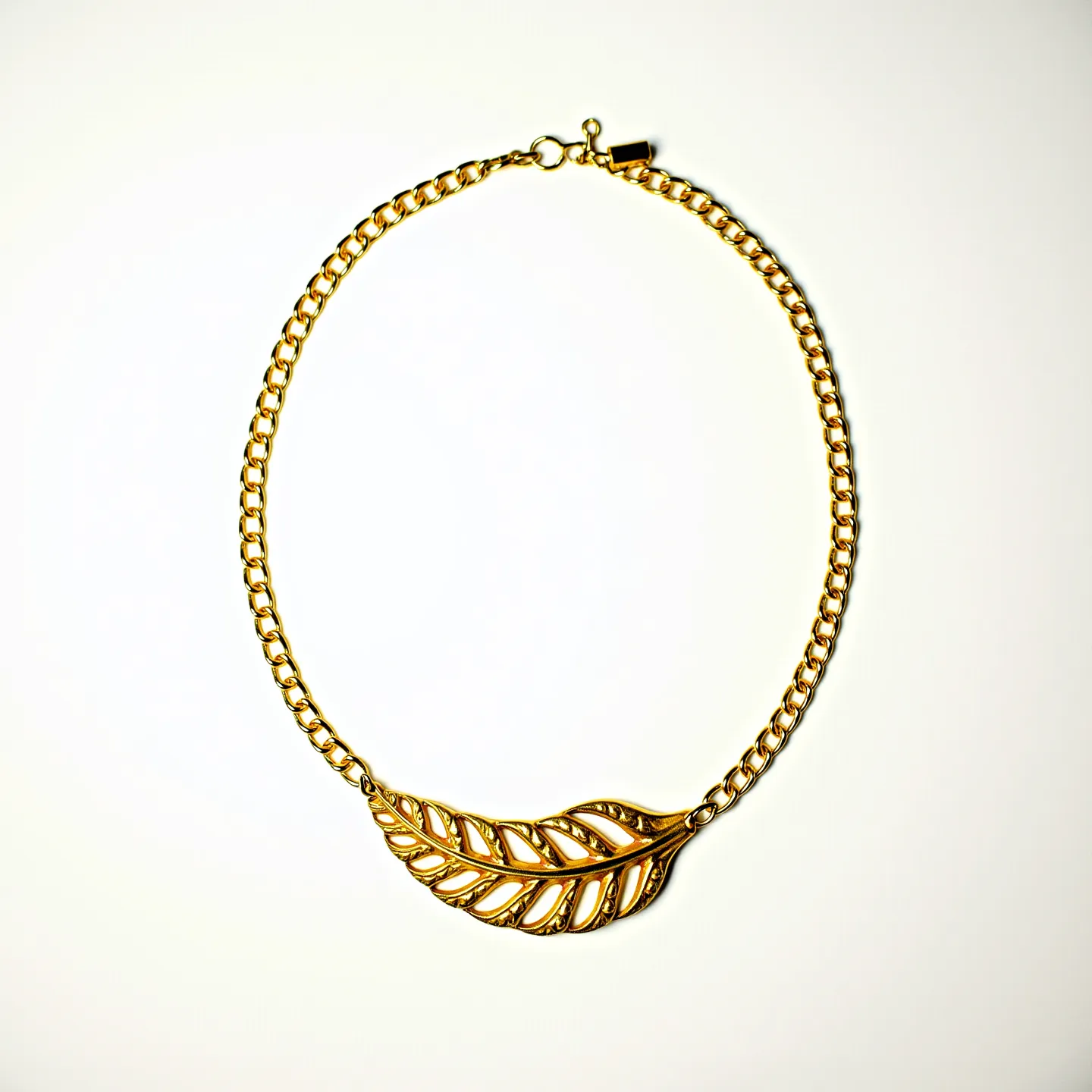 This gold chain necklace features a classic curb link design, composed of interlocking gold links that create a smooth and elegant appearance. At its center, the necklace boasts a detailed gold leaf pendant with intricate cut-out patterns that add a touch of sophistication and artistry. The necklace is finished with a secure toggle clasp, ensuring ease of wear and a reliable closure. The overall design emphasizes both style and versatility, making it a standout accessory for various occasions.