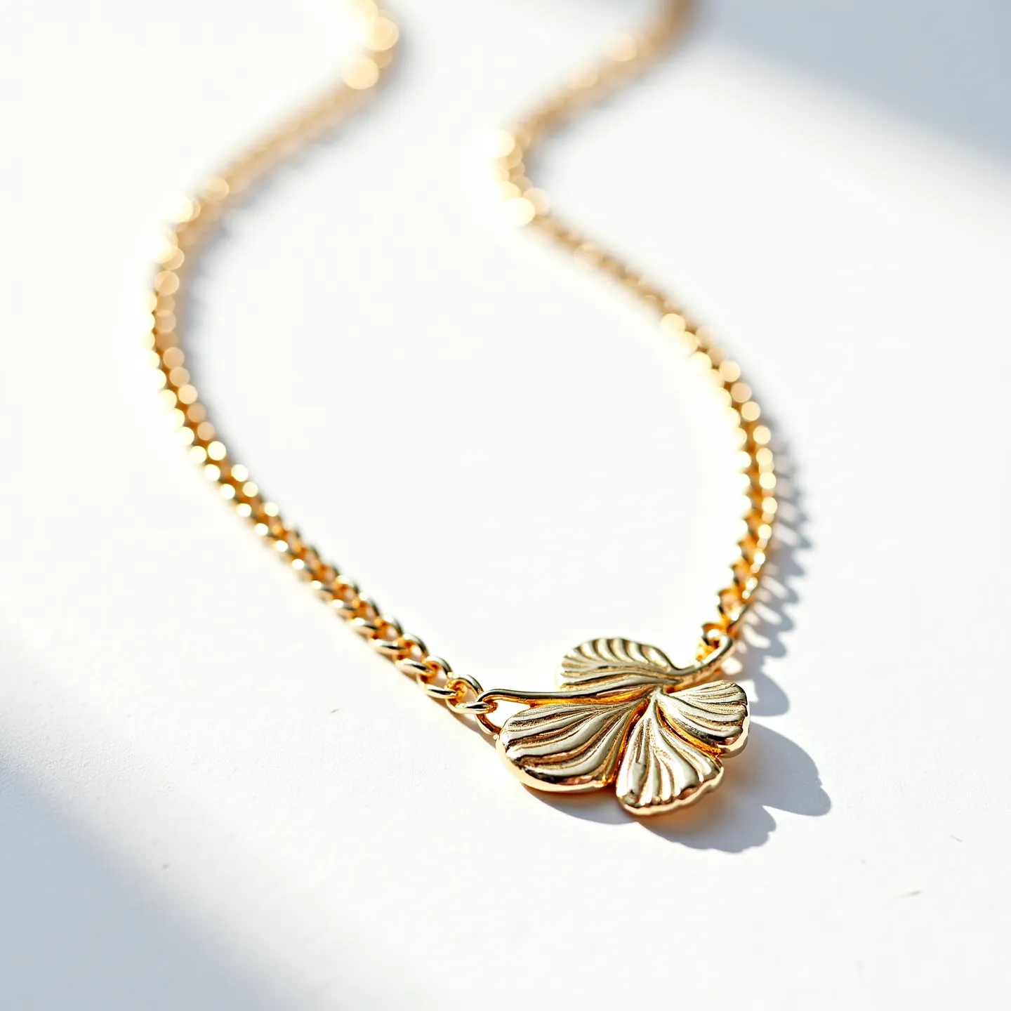 This gold chain necklace features a delicate and intricately designed chain crafted from polished gold links. It showcases a central pendant in the shape of a stylized clover or floral design, without any visible gemstones, enhancing its elegant simplicity. The pendant is integrated seamlessly into the chain, suggesting a well-considered aesthetic choice. A subtle clasp is likely present to secure the necklace when worn, although it is not visible in the current view. The overall presentation of the necklace indicates a refined piece, suitable for both formal and casual occasions, with a focus on the elegance of the gold material and the artistic design of the pendant.