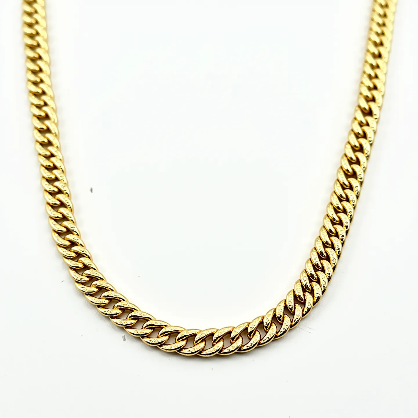 This gold chain necklace features a classic curb link design, showcasing tightly interlocked links that create a smooth, continuous line. The material appears to be gold, giving the chain a rich, lustrous appearance. Each link is uniform in size, contributing to the necklace's elegant and cohesive look. The necklace has a polished finish, enhancing its shine and appeal. The clasp or attachment is not visible in this view, so further details on its design cannot be provided. Overall, this gold chain necklace exhibits a timeless style suitable for various occasions.