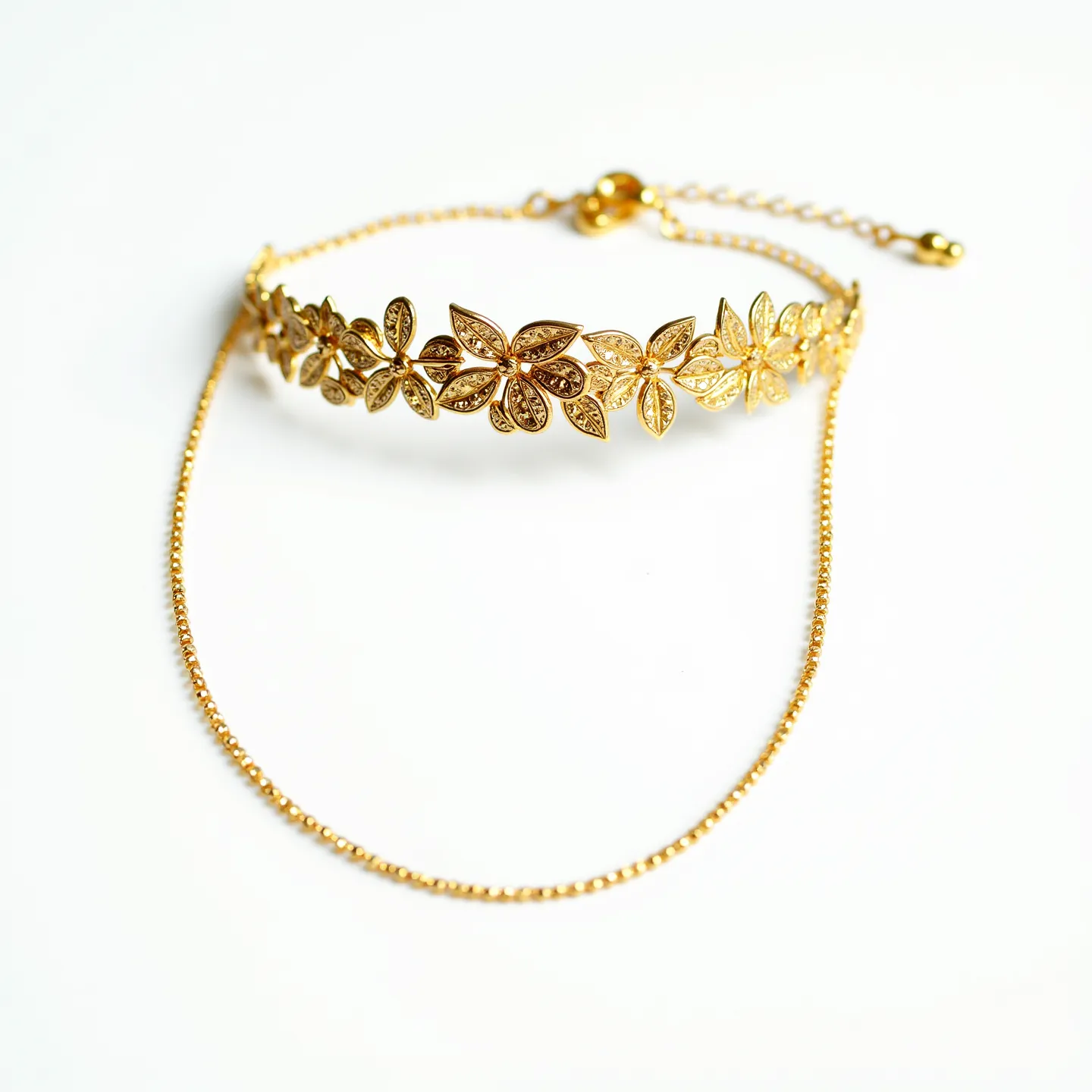 This gold choker necklace features an intricate design of floral motifs interconnected in a continuous pattern, each flower crafted meticulously from gold. The leaves and petals exhibit detailed textures, enhancing the necklace's elegance. The chain is delicate yet sturdy, complementing the floral design with its fine links. The necklace is secured with an adjustable clasp, allowing for a customized fit. The overall look combines artistry and elegance, making it a standout accessory.