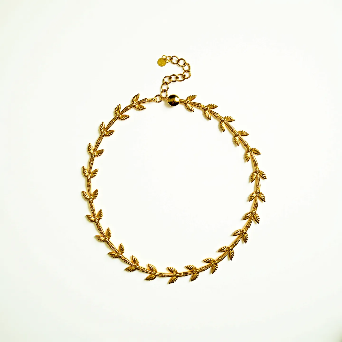 This gold choker necklace features a delicate design composed of interlinked leaf-like motifs that create a continuous and elegant pattern. The necklace is crafted from a polished gold material, which lends it a luxurious and refined appearance. Each leaf is intricately detailed, enhancing the overall texture and artistry of the piece. The choker is fastened with an adjustable chain and a small clasp, allowing for a secure and customizable fit around the neck. The simplicity of the clasp complements the intricate design of the necklace, ensuring both functionality and aesthetic appeal.
