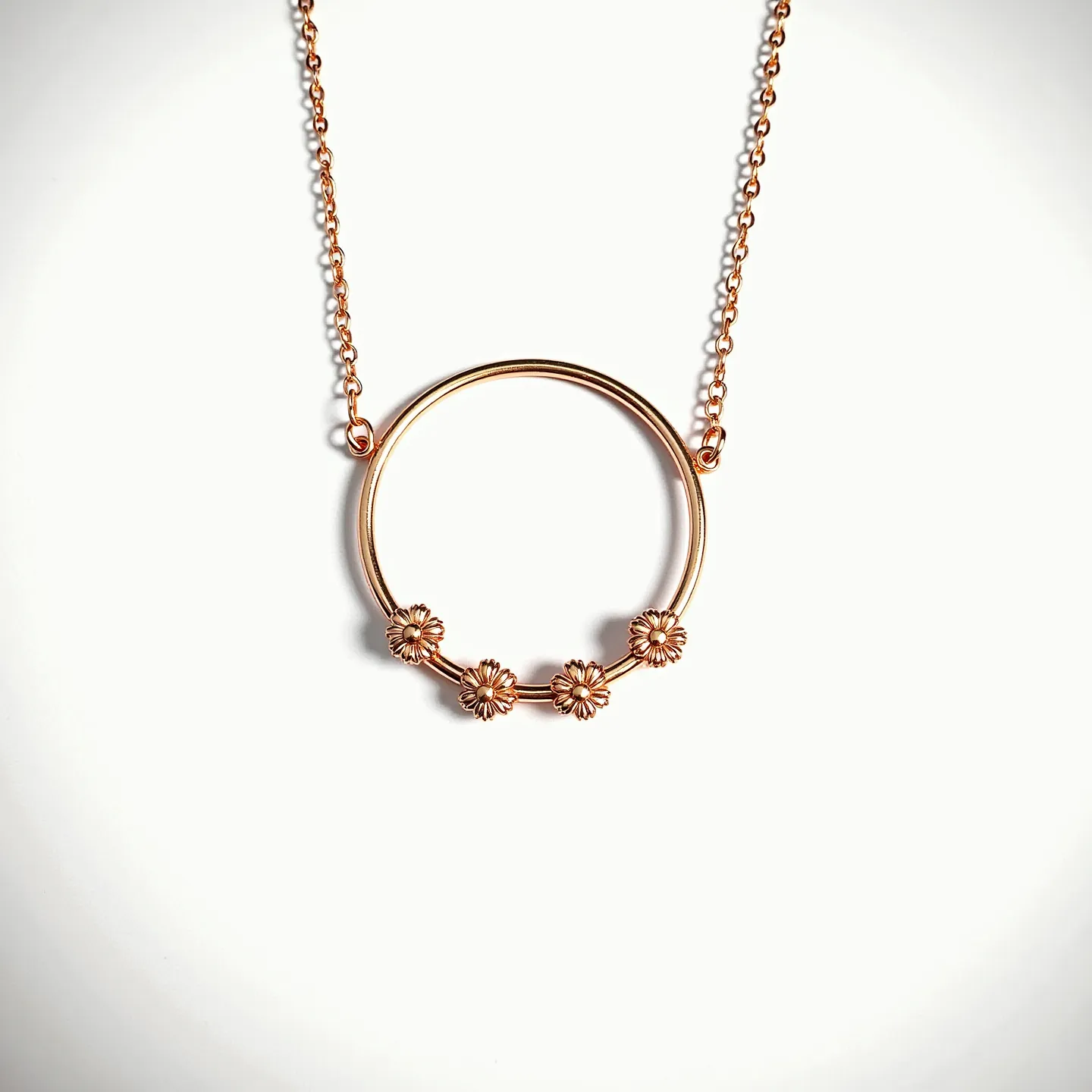 This gold circle necklace features a delicate circular pendant adorned with five intricately detailed flower motifs along the lower curve, adding a touch of elegance and charm. The necklace is crafted from gold, giving it a lustrous and sophisticated appearance. The chain is fine and seamlessly connects to the circle via two small loops at each side. The flowers appear as part of the pendant design, accentuating the overall aesthetic with their finely worked petals. The necklace likely includes a standard clasp for secure fastening, although it is not visible here.