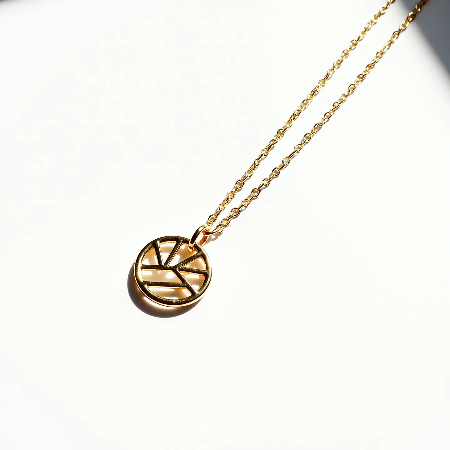 This gold circle necklace features a pendant composed of a series of sleek, geometric cutouts within a circular frame, exuding a modern and minimalist style. The pendant, made of polished gold, hangs from a delicate, finely linked gold chain that adds elegance and complements the warm hue of the pendant. The necklace is secured by a small, discreet clasp that ensures a seamless and secure fit when worn. The overall design showcases a harmonious blend of simplicity and sophistication, making it a versatile accessory suitable for various occasions.