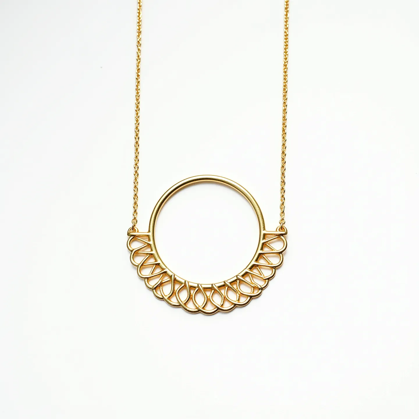 This gold circle necklace features a delicate and elegant design, crafted from high-quality gold material. The necklace consists of a thin, circular pendant with an intricate, scalloped pattern resembling lacework, elegantly adorning the lower half of the circle. This intricate detailing showcases the craftsmanship and adds a touch of sophistication to the piece. The necklace is attached to a fine gold chain, seamlessly connected to the pendant through small loops, ensuring the design stays prominent. The chain's fine texture complements the pendant's elaborate details, creating a harmonious and refined look.