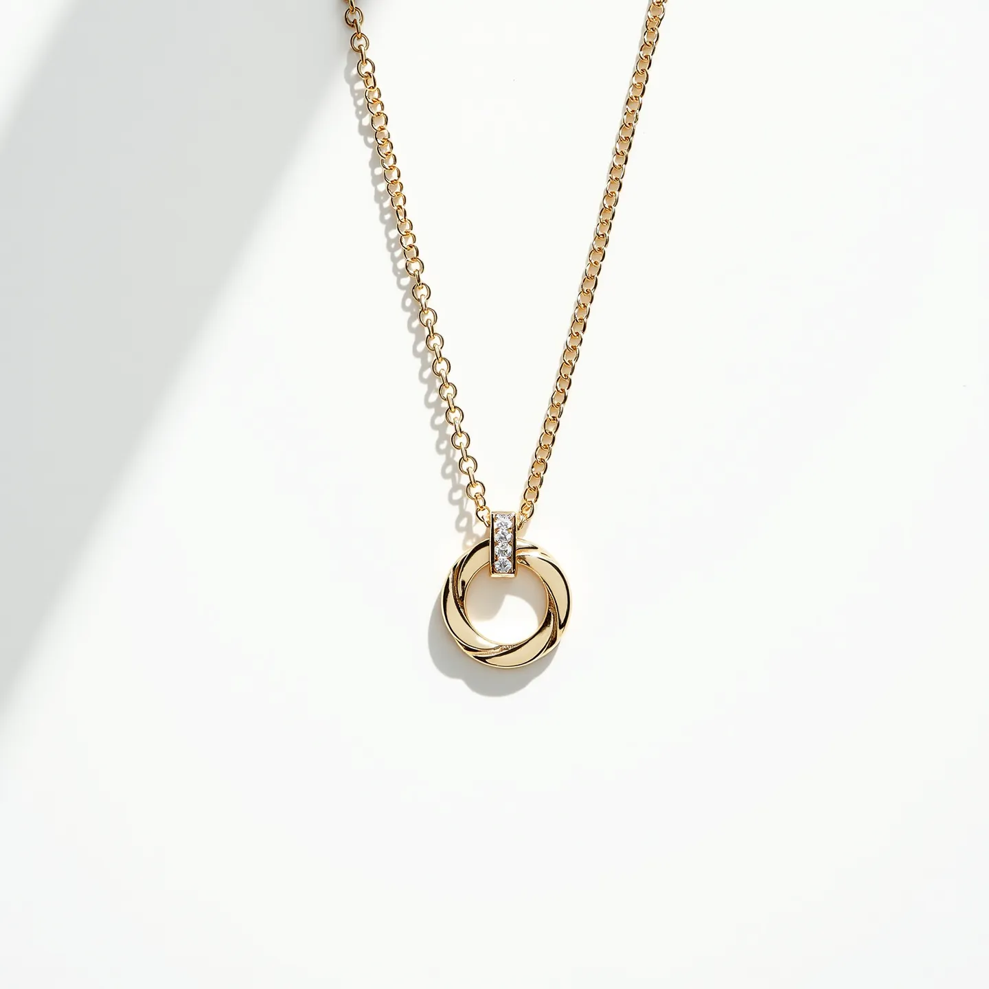 This gold circle necklace features an interlocking circle pendant crafted from polished gold. The pendant is elegantly suspended using a small, rectangular bail that is adorned with a row of sparkling, round-cut gemstones, likely diamonds, set closely together in a channel setting. The pendant hangs from a delicate gold chain with evenly spaced links, providing a refined and cohesive look. The necklace is designed to offer a subtle yet sophisticated accent to any ensemble.