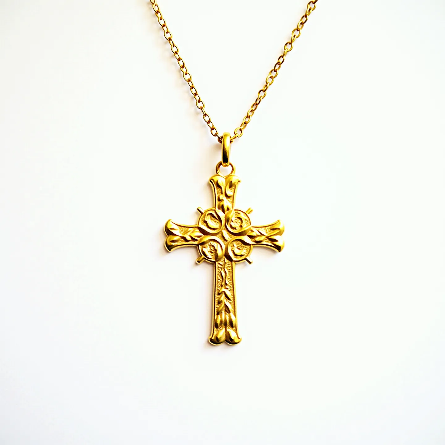 This gold cross necklace features a finely crafted cross pendant with intricate designs and subtle embellishments in its form, likely made of gold or gold-plated material. The cross has a decorative motif that adds an ornate touch, creating a unique texture and aesthetic appeal. The necklace includes a delicate gold chain linked to a loop at the top of the cross, providing a seamless attachment. The necklace's overall design is elegant, offering a timeless and sophisticated look suitable for various occasions.