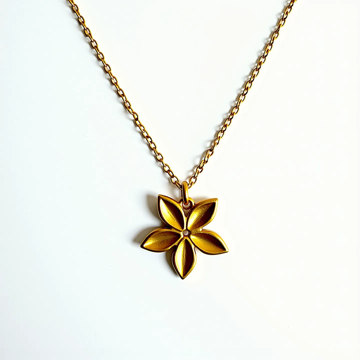 This gold flower necklace features a beautifully crafted flower pendant with five petals, each gracefully shaped to create a sense of elegance and simplicity. At the center of the flower is a subtle indentation that adds a touch of depth to the design. The pendant is made from a polished gold material, giving it a lustrous finish that accentuates the delicate petal details. It is attached to a fine gold chain, which complements the pendant's refined appearance. The chain is secured with a standard clasp, ensuring both functionality and security.