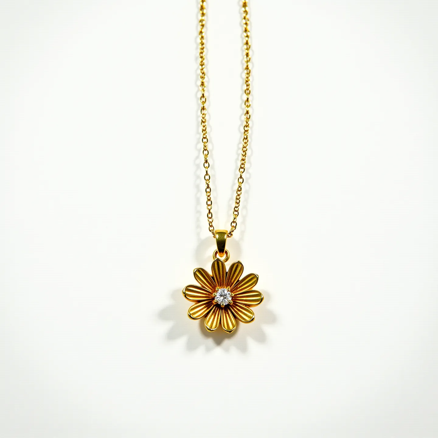 This gold flower necklace features a delicate, intricately designed floral pendant crafted from polished gold, showcasing a series of elegantly curved petals. At the center of the flower, a small, brilliant-cut gemstone, likely a diamond, is securely set in a prong setting, adding a touch of sparkle to the piece. The pendant hangs gracefully from a fine gold chain, which appears to have a simple yet secure attachment at the top of the flower, allowing for a seamless and elegant drape around the neck.