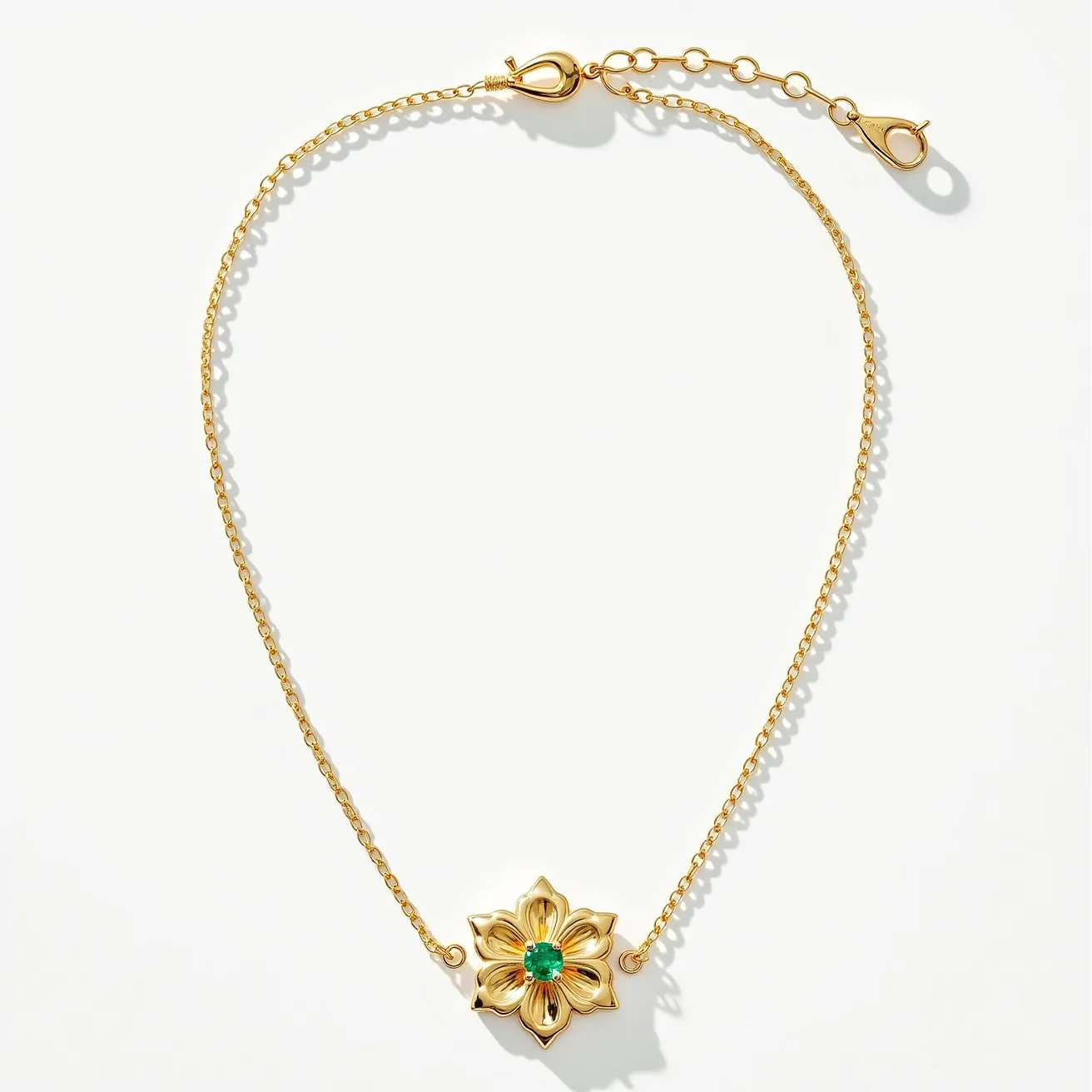 This gold flower necklace features a delicate floral pendant crafted from gold, showcasing intricate detailing in the petals. At the center of the flower, there is a round green gemstone, set in a secure prong setting that enhances its vibrant hue. The necklace chain is a fine gold link design, complementing the elegance of the pendant. It is equipped with a lobster clasp, providing both security and ease of wear, along with an adjustable chain section for flexible fit.