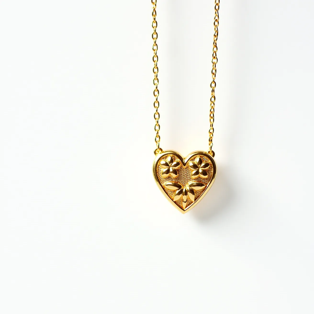 This gold heart necklace features a beautifully crafted pendant made from polished gold. The heart-shaped pendant is adorned with an intricate floral design, adding a touch of elegance and sophistication. The chain is composed of delicate, evenly spaced links, ensuring both strength and style. The necklace is likely secured by a standard clasp mechanism, which provides ease of wear and security. The overall design exudes a classic and timeless aesthetic, perfect for any occasion.