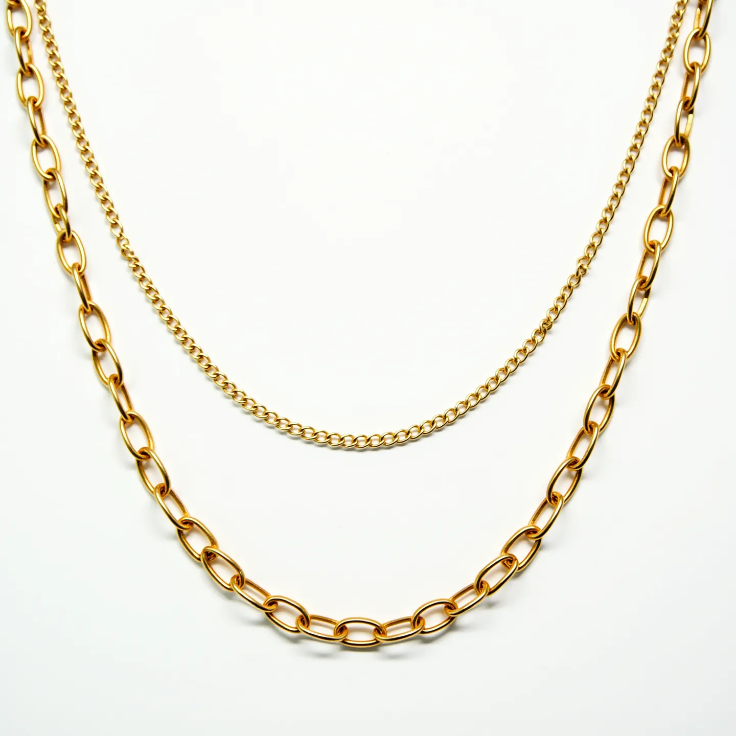 This gold link necklace features two distinct styles of chains: a thicker link chain and a finer, tightly interwoven chain. The thicker chain consists of oval links, which are polished to a high shine, reflecting light elegantly. The finer chain has small, closely connected links that create a more delicate and continuous flow. Both chains are made of gold, contributing to their luxurious appearance. The necklace is designed without any gemstones, enhancing its classic and timeless appeal. Additionally, a standard lobster clasp secures the necklace, offering functionality and ease of use.