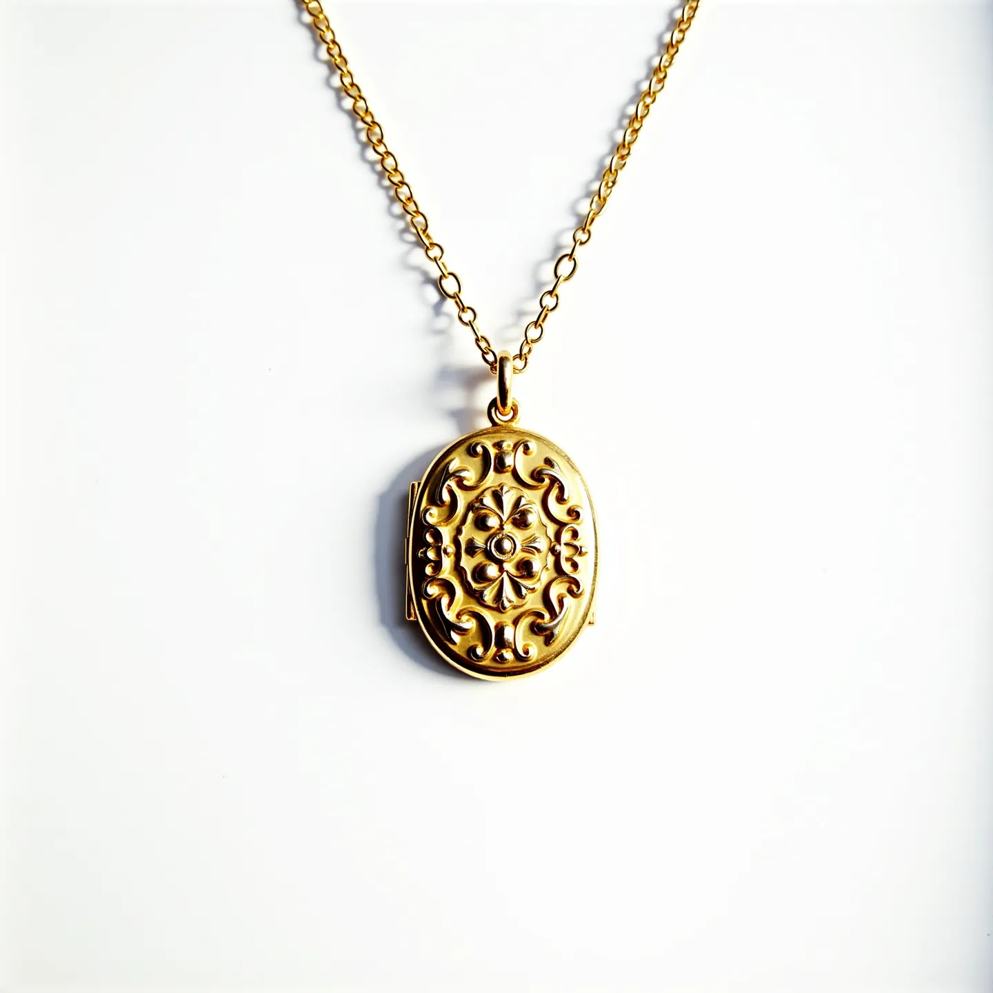 This gold locket necklace features an intricately designed oval-shaped pendant crafted from what appears to be polished gold, displaying an ornate pattern with floral and scroll motifs. At the center of the locket, there is a small, round gem that could possibly be a diamond or a similar stone, secured with a prong setting. The locket hangs from a delicate gold chain, composed of interconnected oval links giving it a classic yet elegant appearance. The necklace is fastened with a sturdy spring ring clasp, ensuring ease of wear and security.