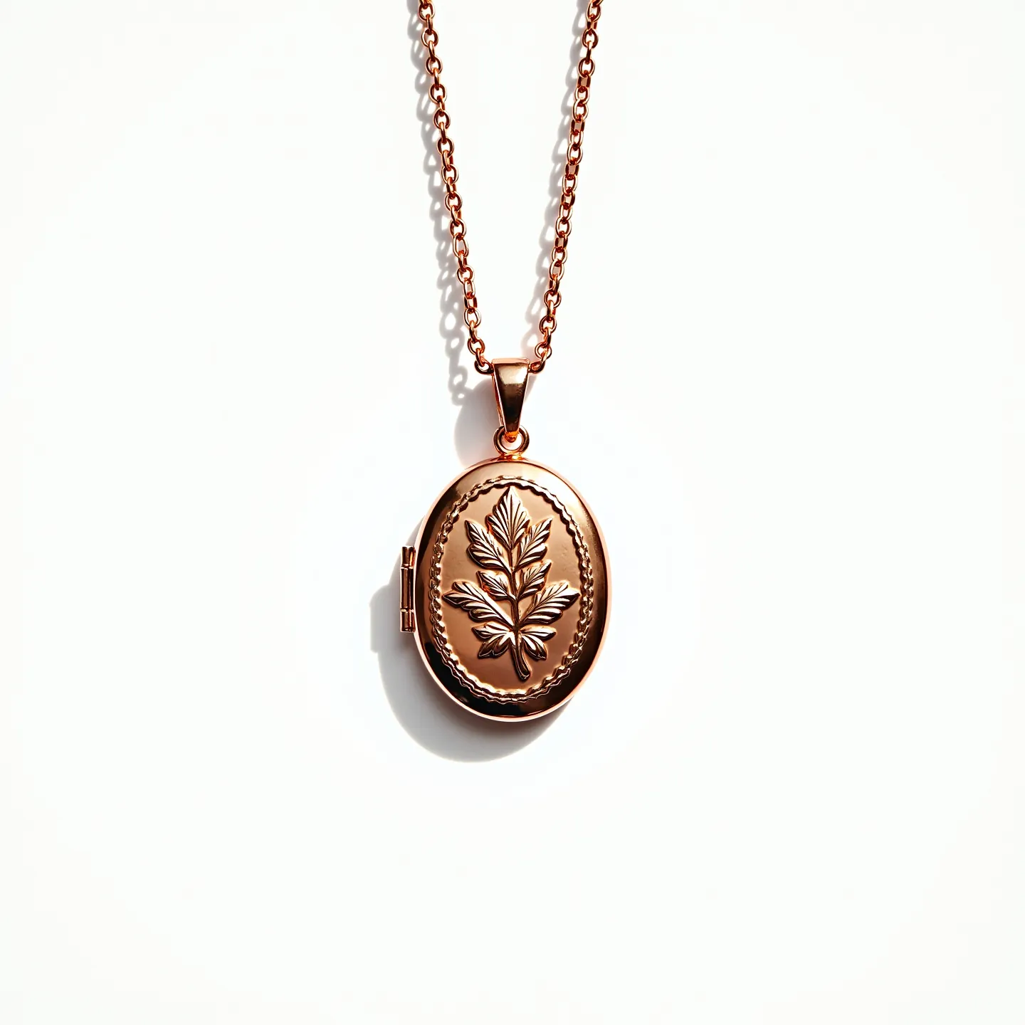 This gold locket necklace features an oval-shaped pendant crafted from polished gold. The front of the locket is intricately embossed with a botanical design, showcasing a detailed leaf motif encircled by a delicate border. The locket is suspended from a classic gold chain composed of interlinked round links, which provide a secure and streamlined appearance. The attachment consists of a graceful bail that connects the locket to the chain, ensuring it hangs securely and attractively.