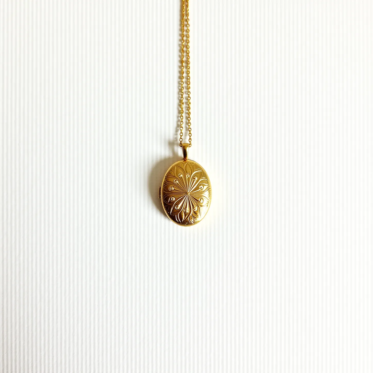 This gold locket necklace features an oval-shaped pendant crafted from gold, showcasing an intricate engraved design that adds a touch of elegance. The pattern on the locket is accented with small, round-cut gems set subtly within the design, enhancing the overall allure. Suspended from a delicate gold chain, the necklace exudes a classic and timeless appeal. The chain appears to be a simple link style, complimenting the refined look of the pendant. The locket is attached via a small, unobtrusive bail, seamlessly connecting it to the chain and ensuring secure wear.