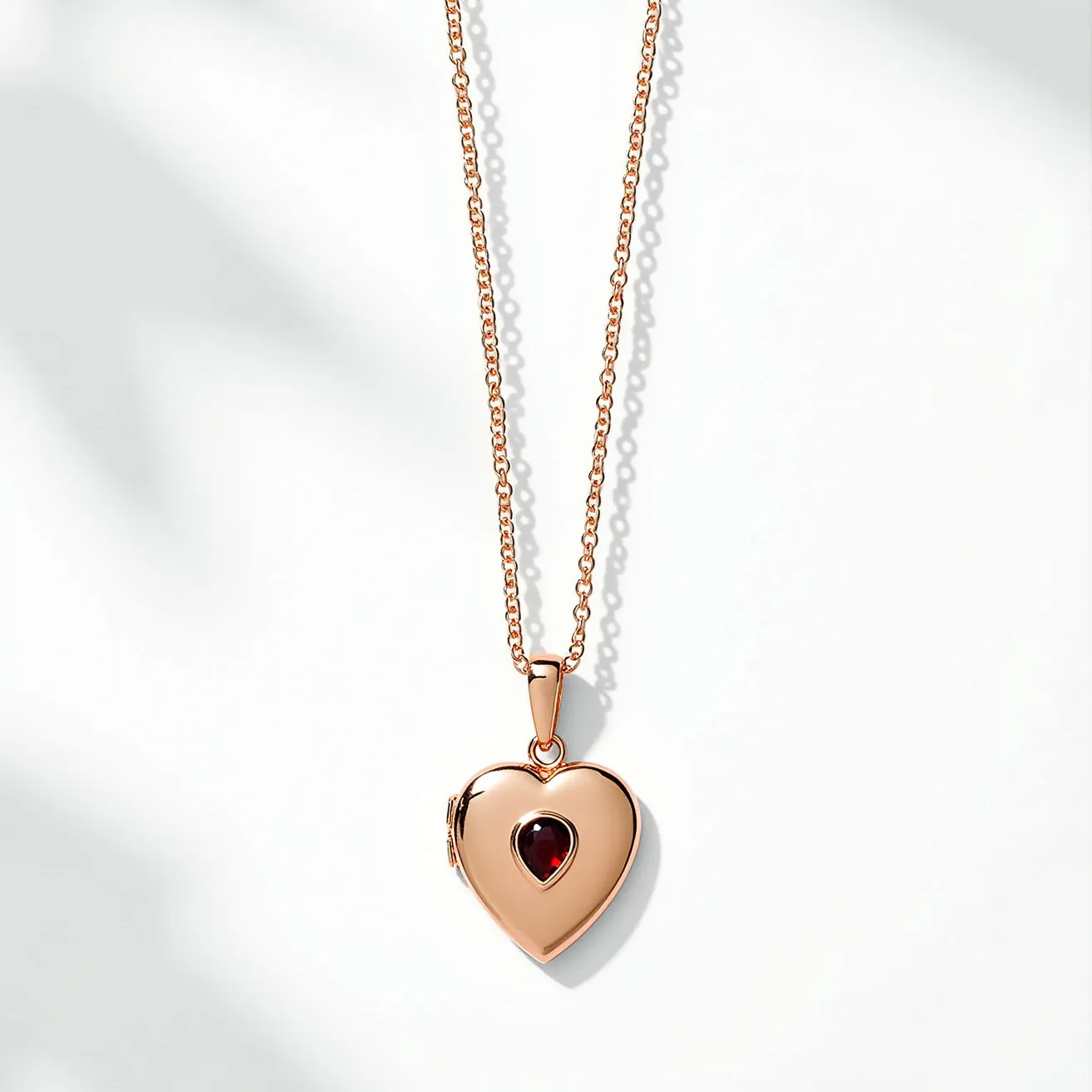 This gold locket necklace showcases a heart-shaped locket crafted from polished gold, featuring a centrally set, oval-cut gemstone that appears to be a deep red garnet or similar stone. The gemstone is elegantly bezel-set, providing a secure and stylish presentation. The necklace is completed with a classic chain composed of interlocking links, which connects to the locket through a simple, gold bale. The closure mechanism is likely to be a standard lobster clasp or similar attachment, ensuring ease of wear and security.