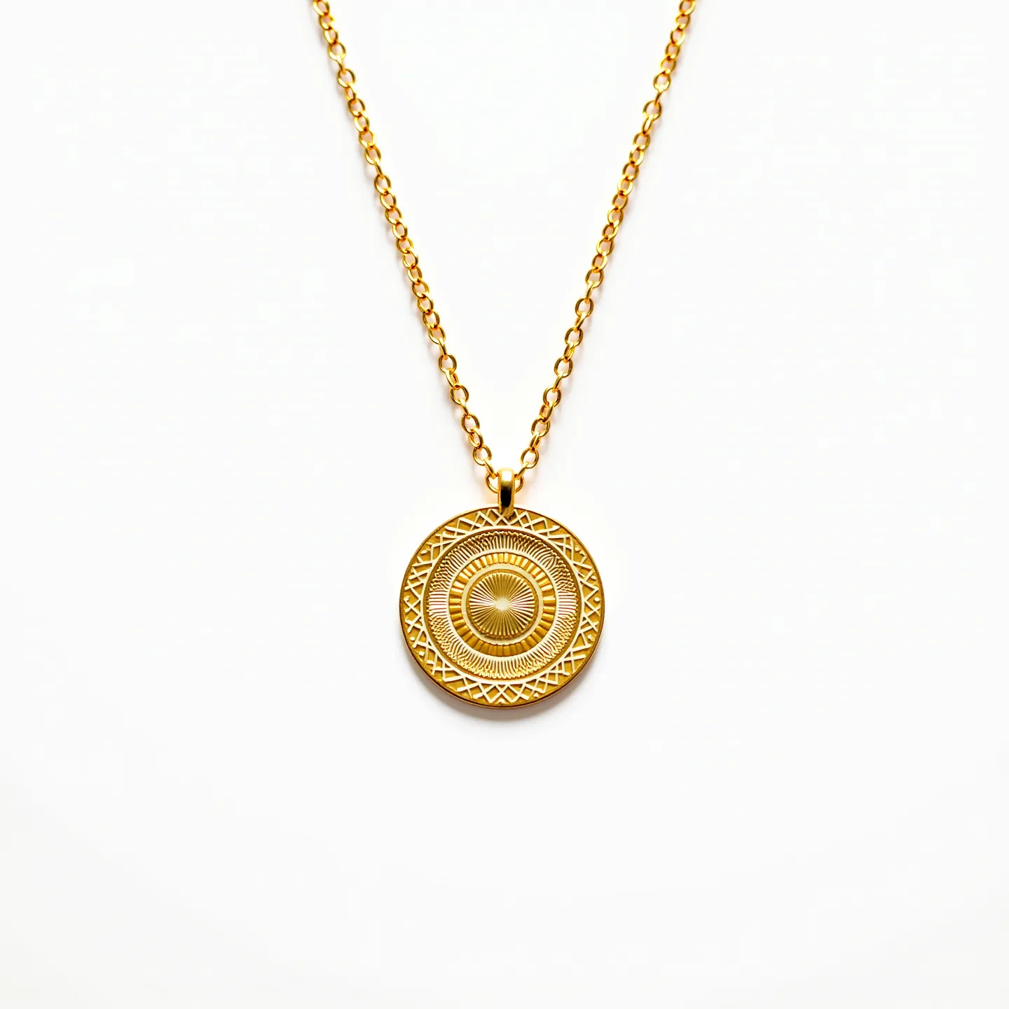 This gold medallion necklace features a round pendant with intricate, symmetrical patterns etched into its surface, adding an element of detailed craftsmanship. The design consists of concentric circles and geometric shapes, creating a sunburst effect that radiates from the center. The medallion hangs from a gold chain composed of small interlocking links, offering a delicate yet secure structure. The necklace is completed with a simple bail for attachment, ensuring that the pendant stays centered and secure along the chain.