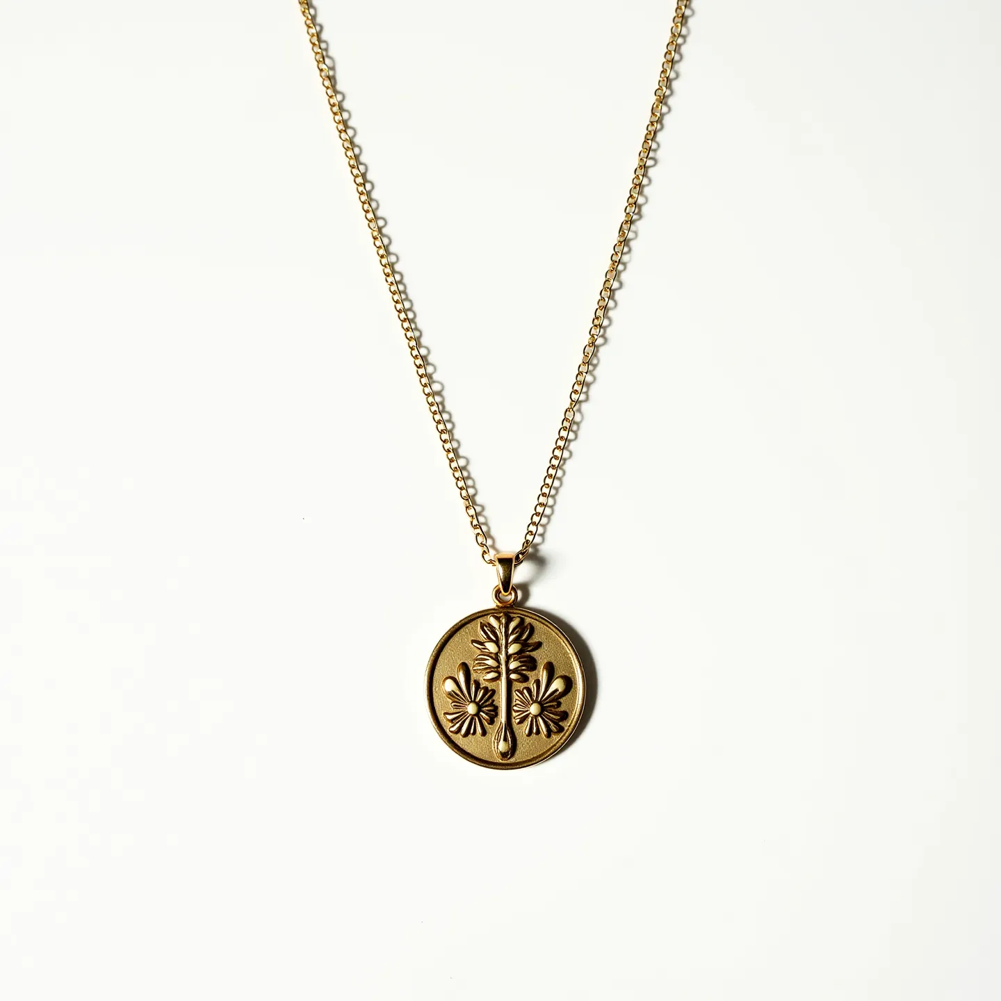 This gold medallion necklace features a finely crafted round pendant with an engraved floral design. The medallion is suspended from a delicate cable chain, which showcases a consistent link pattern, enhancing the elegance of the piece. The gold used in both the chain and medallion gives a rich and warm hue, indicating it is likely crafted from high-quality metal. This necklace is affixed with a standard spring ring clasp, ensuring secure wearability. The overall design emphasizes simplicity and sophistication, with the floral engraving adding an element of artistic detail.