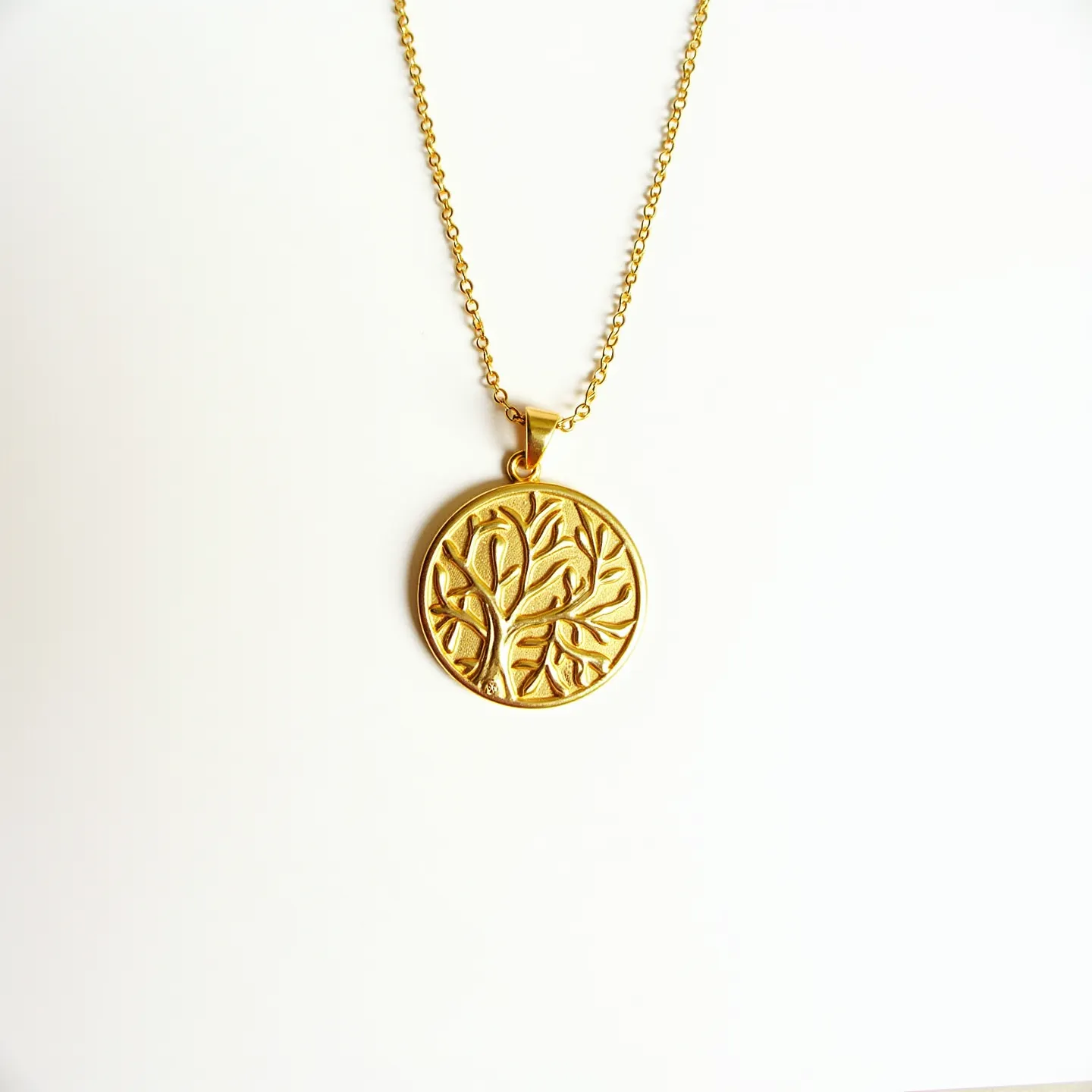 This gold medallion necklace features a beautifully crafted circular pendant with an intricate tree design, symbolizing growth and strength. Made of a polished gold material, the pendant captures light with a warm, lustrous glow. The tree design is embossed into the medallion, adding depth and texture to the piece. The necklace is secured by a delicate chain that complements the medallion's elegance. The chain is linked to the pendant via a secure bail that allows for smooth movement and flexible wear. An elegant clasp ensures a secure fit, making this necklace both a stylish and symbolic accessory.