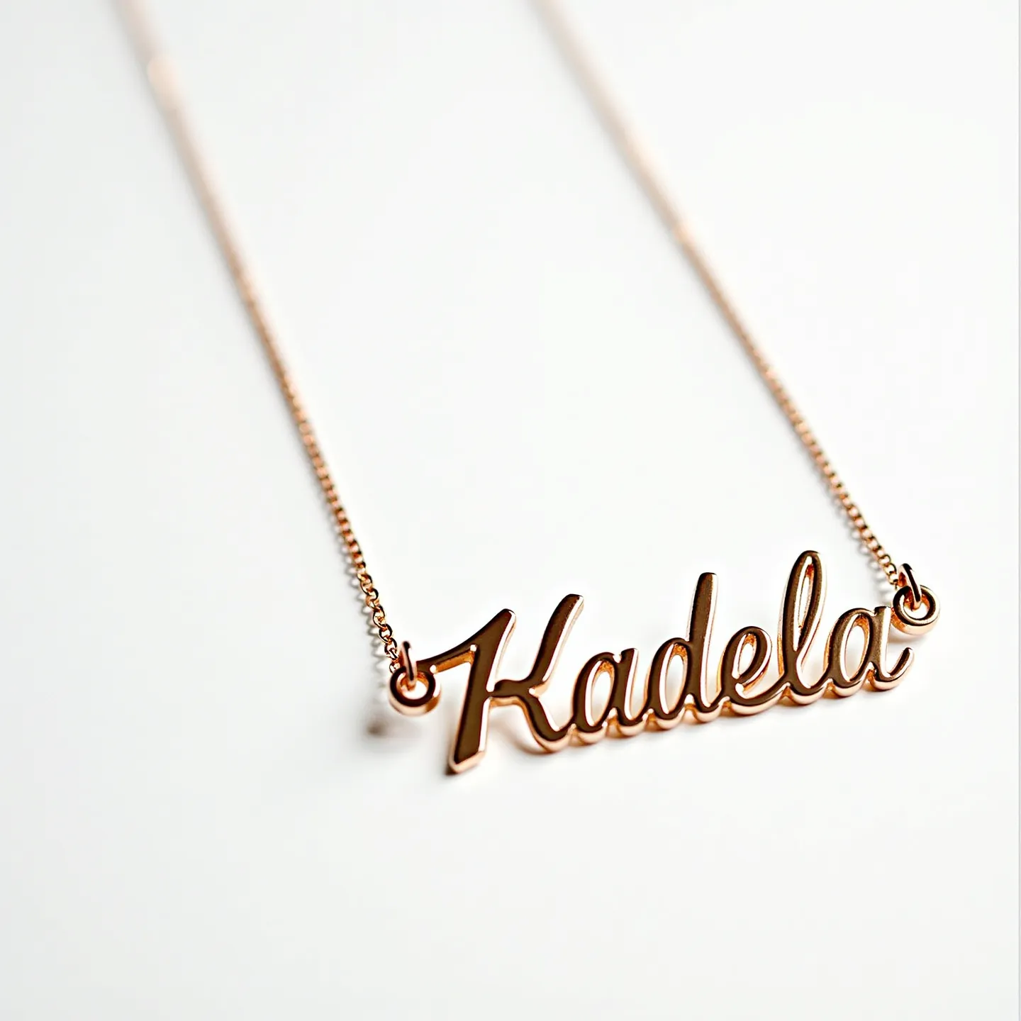 This gold name necklace features the word "Kadela" elegantly crafted in a cursive script, highlighting its personalized design. The necklace appears to be made from gold, giving it a luxurious and shiny appearance. The letters are smoothly finished and linked to a delicate chain that complements the overall design. The nameplate is connected to the chain with small gold loops, ensuring secure attachment. The chain is likely to feature a simple clasp mechanism that would be typical for such necklaces, allowing for easy wear and removal.