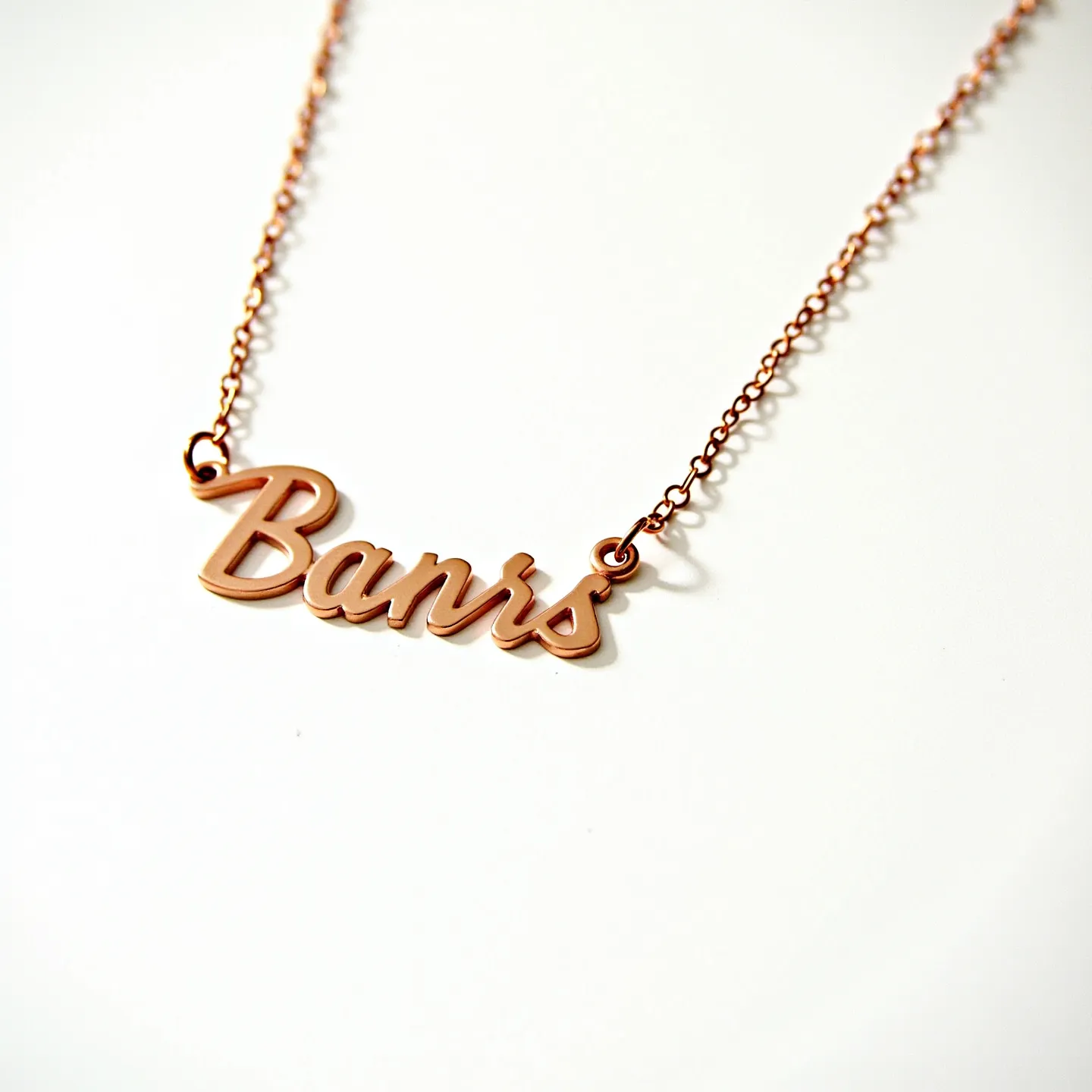 This gold name necklace features a polished, elegant script spelling out a name, crafted from gold. It is attached to a delicate gold chain that seamlessly links to the nameplate via small rings, ensuring a coordinated and cohesive design. The necklace appears to possess a simple yet classic structure without additional embellishments or gemstones, focusing on the sleek, lustrous quality of the metal itself. The overall design exudes a timeless charm, ideal for everyday wear or as a personalized gift.