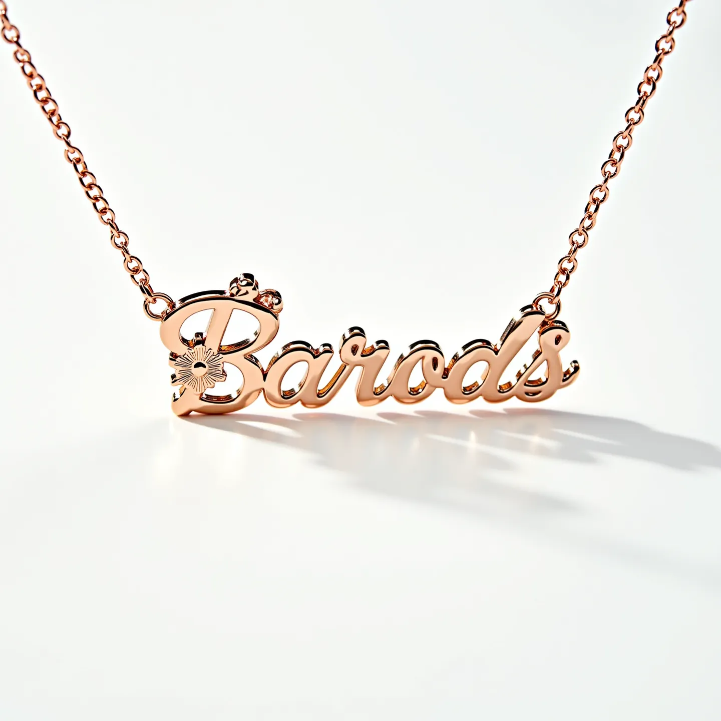 This gold name necklace features a delicate cursive script spelling out "Barods" with an elegant floral design attached to the initial "B." The necklace is crafted from a warm, shiny gold material that lends it a luxurious feel. The floral design is engraved with intricate detail, adding a touch of artistry to the overall piece. The necklace is connected to a classic chain link, contributing to its timeless design, and it likely features a conventional clasp for secure attachment. The overall design reflects a blend of sophistication and personalized charm.