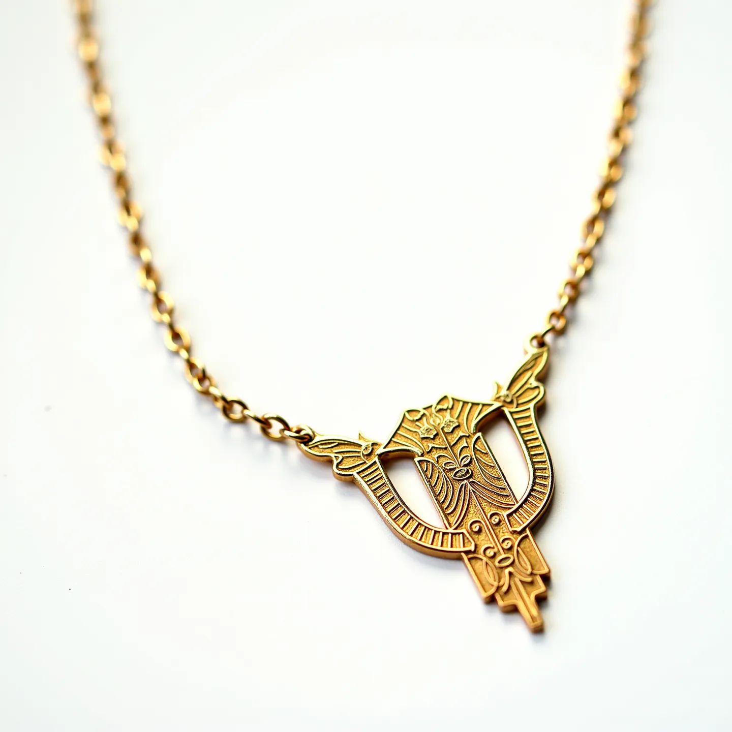 This gold necklace features an intricately designed pendant, crafted with artistic engravings that add to its elegance. Made from polished gold, the pendant has a symmetrical shape that suggests a lyre or an abstract floral motif, enhancing its allure. The necklace's chain is composed of delicate links, providing both strength and a classic appearance. The absence of visible gems emphasizes the artistry of the goldwork itself. The necklace is likely secured with a discreet clasp that blends seamlessly into the overall design, ensuring both functionality and aesthetic appeal.