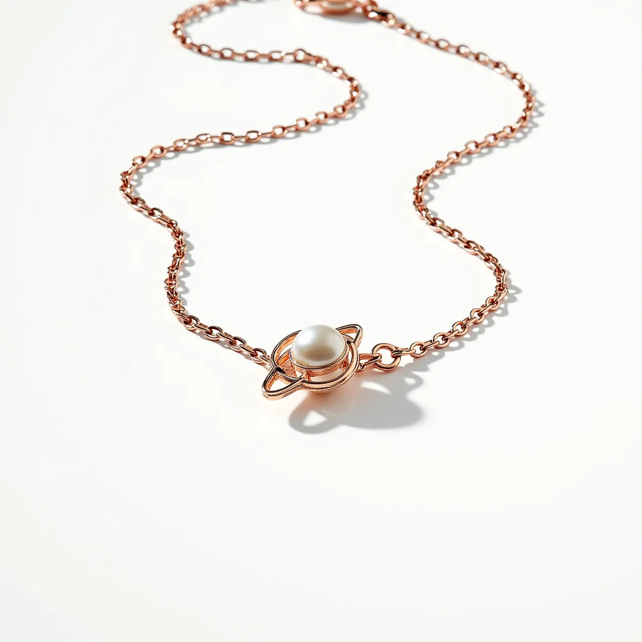 This gold necklace features a delicate rose gold-toned chain that elegantly supports a unique centerpiece designed in the shape of a planet. At the heart of this design is a lustrous white pearl, which is prominently set to mimic the appearance of a planet, with gold-toned rings encircling it, adding to the celestial motif. The pearl boasts a smooth, spherical surface indicative of a high-quality pearl, while the chain itself is composed of interconnected, round links. The clasp mechanism is not visible in the image, but the overall design maintains a thematic focus on elegance and simplicity, uniting the celestial with the refined in a harmonious display.