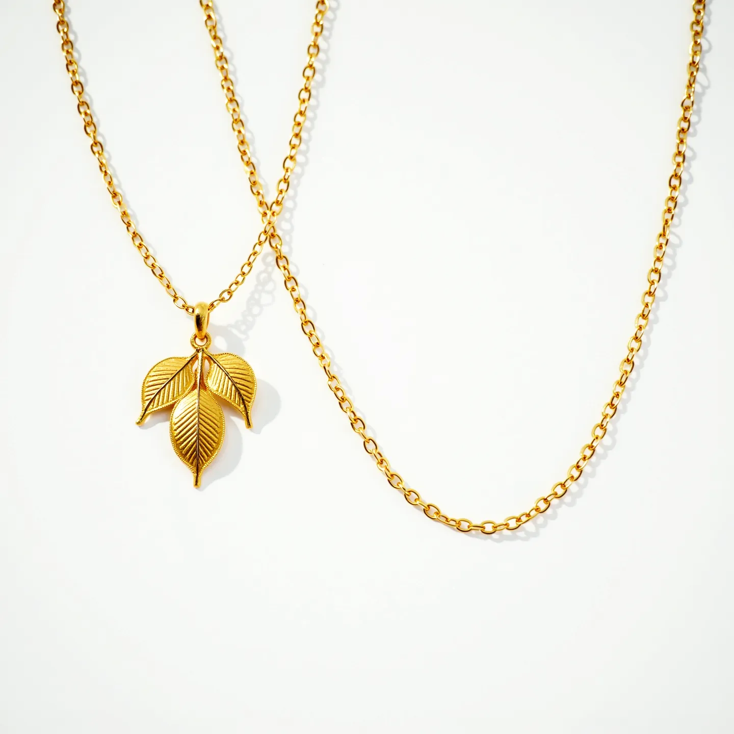 This gold necklace features a delicate chain crafted from a series of small, interlinked loops, conveying a subtle elegance. The highlight of the piece is the pendant, designed as a trio of intricately detailed leaves, each showing fine veins that emphasize their natural inspiration. The pendant hangs from a single loop attached to the chain, adding an artistic and organic touch. This combination of simple yet refined elements creates a classic look, perfect for both casual and formal occasions. The absence of gemstones keeps the focus on the craftsmanship of the gold.