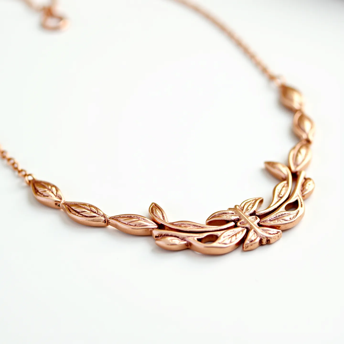 This gold necklace features an intricate leaf design in rose gold, showcasing elegant craftwork with smooth, flowing lines that interweave to create a symmetrical pattern along the chain. The surface of the leaves is adorned with delicate engravings that mimic the vein patterns found in nature, adding texture and depth to the piece. The central motif includes an artfully shaped leaf or butterfly element that draws the eye, serving as the focal point. The necklace is completed with a simple lobster clasp, ensuring secure fastening and ease of wear. The craftsmanship highlights the refined and graceful nature-inspired aesthetics of this piece.