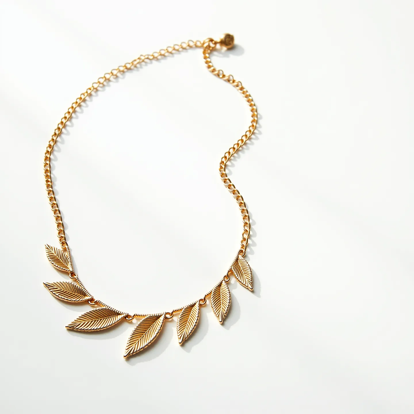 This gold necklace features a series of intricately designed leaf motifs, each linked together to form a graceful and elegant pattern. The leaves are crafted from gold, showcasing detailed vein patterns that add a touch of natural beauty to the piece. The chain is composed of small interlocking gold links, providing both flexibility and strength. The necklace is secured with a simple round clasp at the end, allowing for easy attachment and removal. Its overall design blends nature-inspired elegance with timeless craftsmanship, making it a versatile accessory for various occasions.