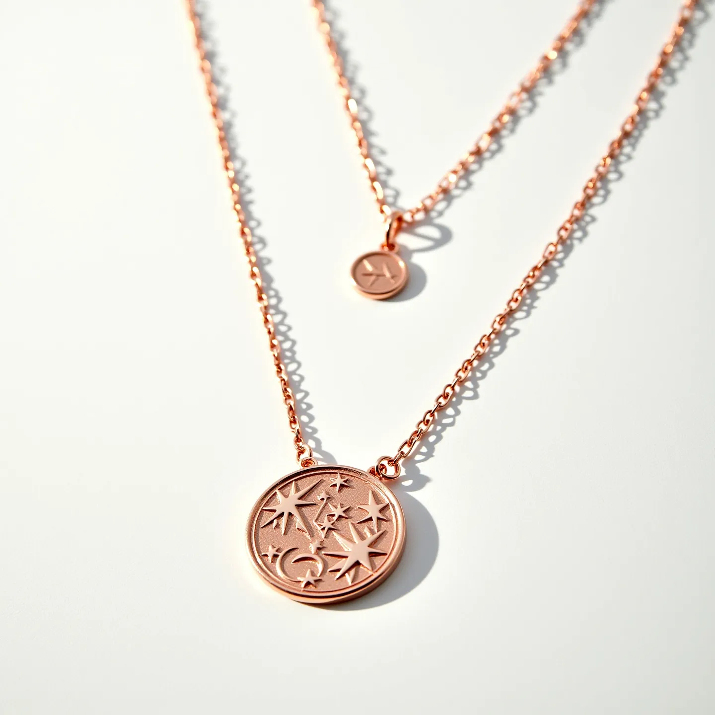 This gold necklace features a delicate and elegant design with a rose gold finish, showcasing two layered chains. The necklace displays two circular pendants, each adorned with celestial motifs including stars and a crescent moon. The larger pendant hangs on the longer chain, while a smaller matching pendant is set on the shorter chain. Both pendants, crafted with fine detailing, are set in a simple bezel setting that enhances their celestial theme. The necklace is likely secured with a lobster clasp, ensuring a secure fit while complementing its refined and simple aesthetic.