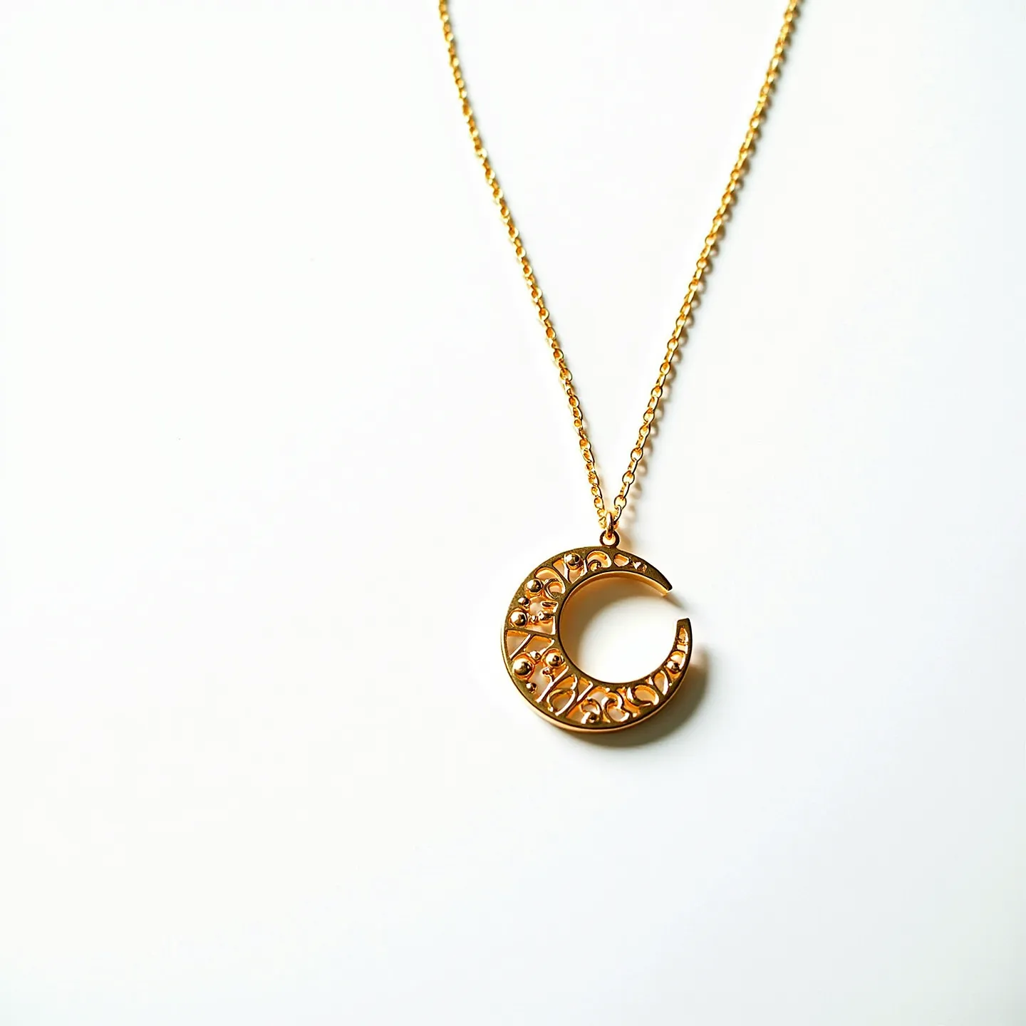 This gold necklace features a delicate chain leading to a crescent moon pendant. The pendant is crafted from gold and intricately designed with small, decorative engravings or embellishments. Several tiny, round stones are embedded along the surface of the crescent, adding a touch of sparkle. These stones appear to be set in a bead or prong setting. The necklace includes a simple clasp for secure attachment, complementing its elegant and understated design.