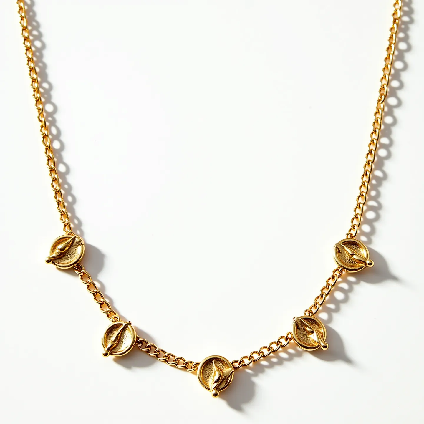 This gold necklace features a series of cowrie shell pendant accents linked along a delicate curb chain. Each shell is crafted from gold, providing a polished and refined appearance. The smooth finish of the metal gives the necklace a luxurious yet understated look. The necklace is likely fastened with a simple clasp, allowing for easy wear while maintaining its elegant design.