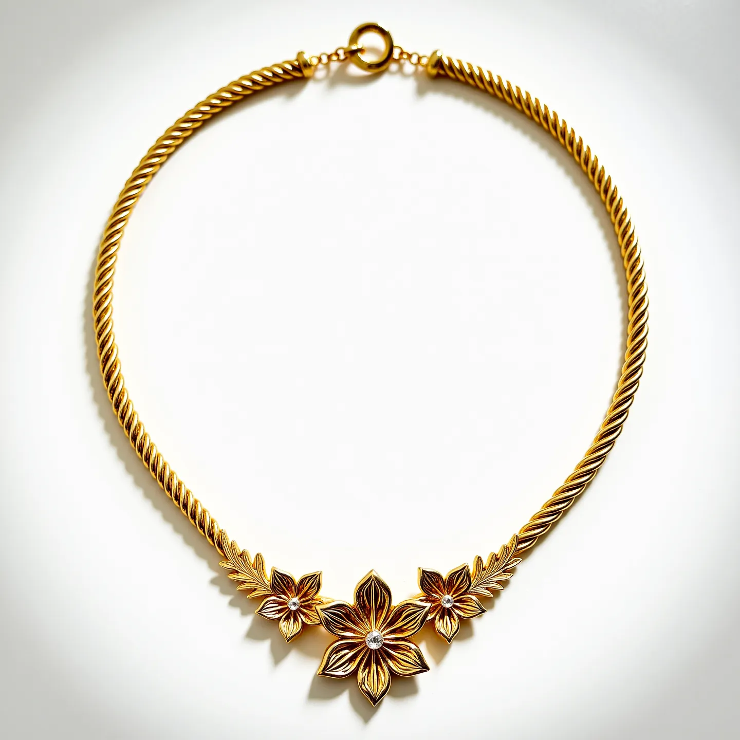 This gold rope necklace is intricately designed, featuring a twisted pattern that adds a dynamic texture to the piece. At its centerpiece, there are three prominent floral motifs, each adorned with a small, round-cut, clear gemstone centrally set, enhancing the elegance of the design. The flowers are detailed with petal accents, and the gemstones are likely set in a bezel style, providing a secure and complementary setting. The necklace is finished with a classic round clasp, ensuring a secure closure and ease of wear. The overall craftsmanship showcases a balance of sophistication and intricate detailing, making it a standout piece.