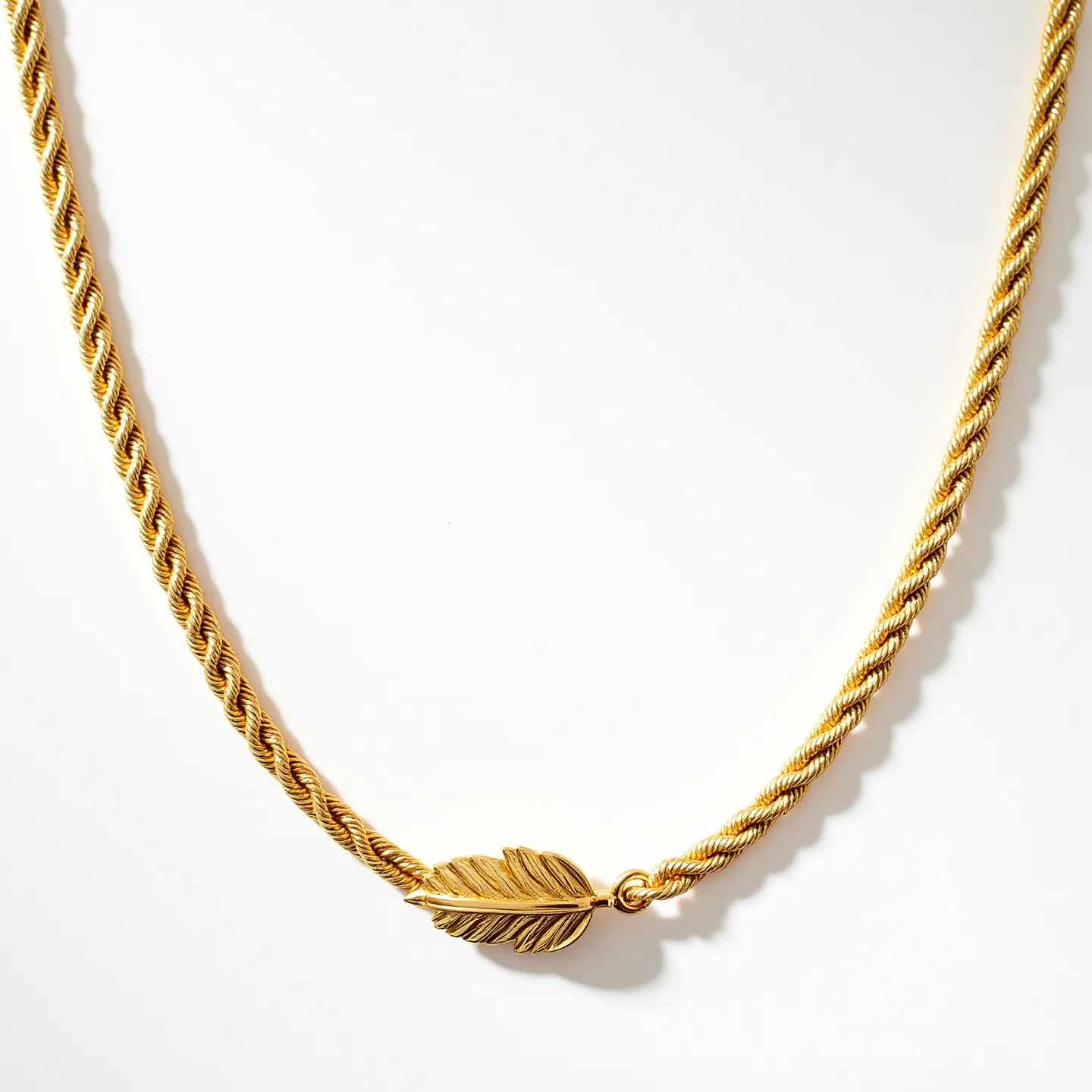 This gold rope necklace features a classic twisted design, giving it a sophisticated and elegant appearance. Crafted from polished gold, the chain showcases a luminous shine, highlighting its luxurious appeal. At its center is a gold feather-shaped attachment, adding a unique and decorative element to the necklace. The clasp is seamlessly integrated, ensuring both style and functionality. The necklace's weight and texture suggest a high-quality fabrication, making it not only a beautiful accessory but also a piece designed for durability and lasting wear.