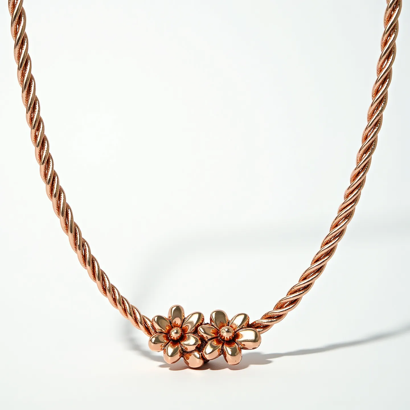 This gold rope necklace features a twisted design, highlighting the luxurious texture of the metal. At its center, there are two flower-shaped ornaments adding a touch of elegance and charm. Each flower appears to be intricately crafted, possibly housing a small gemstone or detailed gold work in its core, though specifics about the stones cannot be determined from the image. The necklace seems to employ a seamless construction, as there is no visible clasp from this view, suggesting an artistic blend with the rope design.