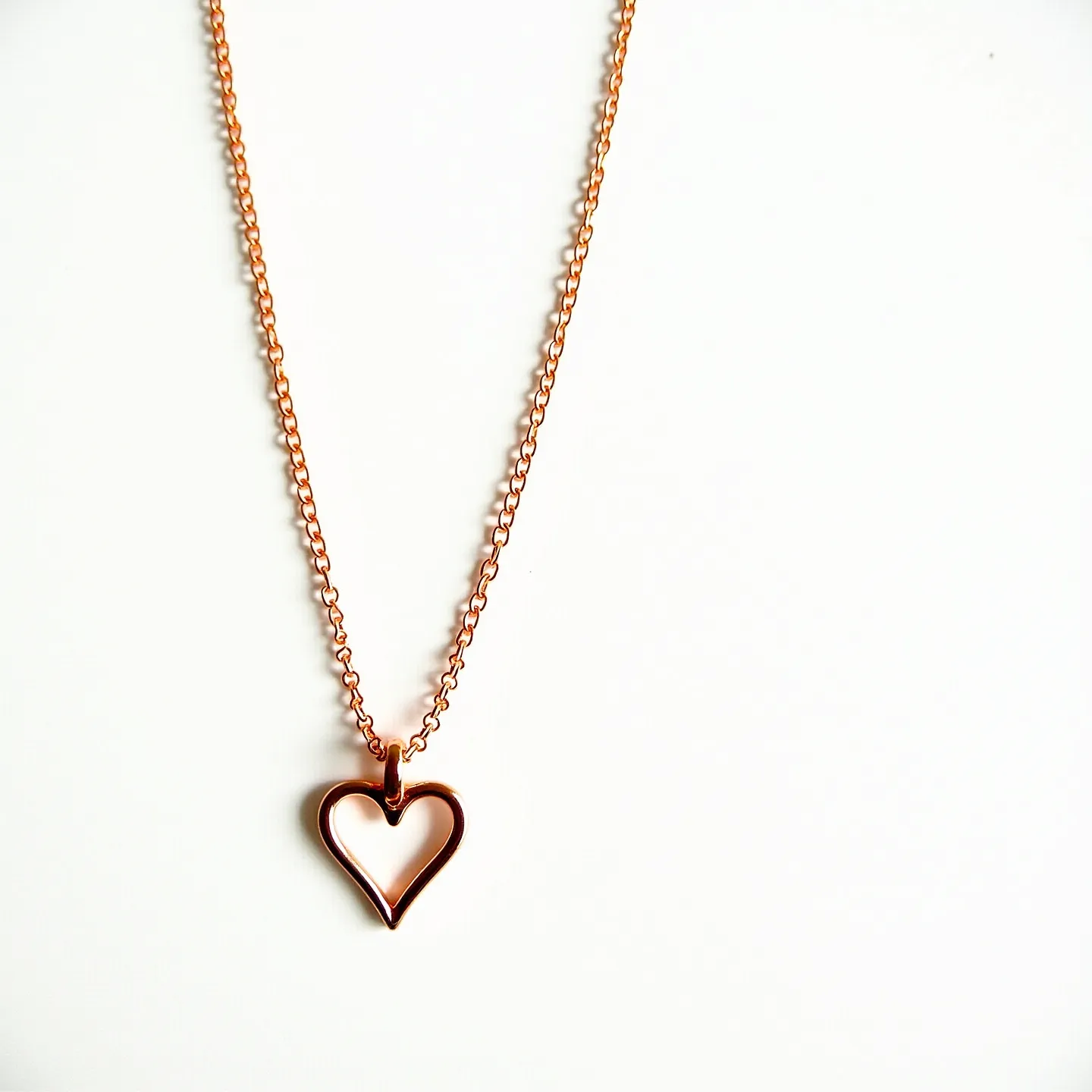 This heart chain necklace features a delicate, small-link chain that appears to be crafted from rose gold or a similar metallic finish. The pendant is an elegant open heart design, matching the chain in color and material, suggesting a cohesive and polished look. The heart is suspended from a simple loop, allowing it to hang freely and move naturally with the wearer. The necklace is likely to have a standard clasp for easy wearability, although it is not visible in the image. The simplicity of the design emphasizes the elegant use of materials and the symbolic heart motif.